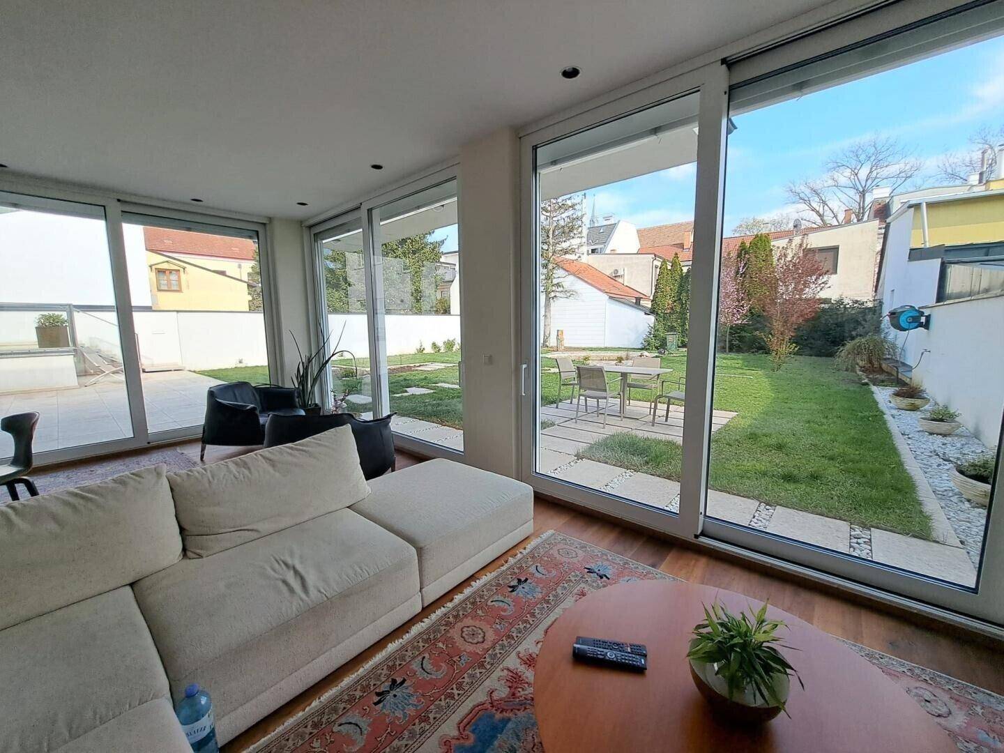 Helles Wohnzimmer mit bequemer Couch, Holzboden und großen Fenstern zum Garten.