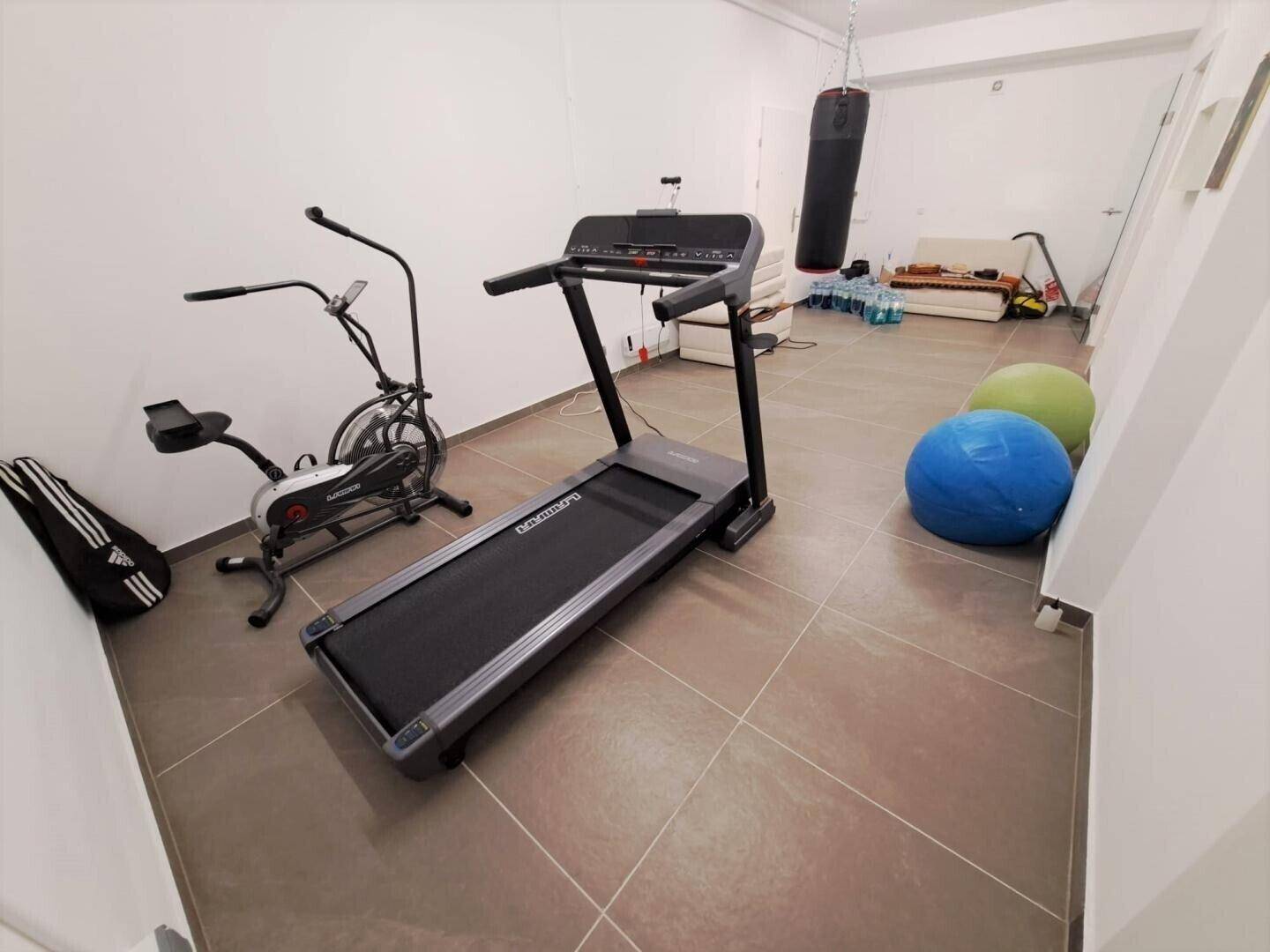 Geräumiger Fitnessraum im Untergeschoss mit Laufband, Boxsack und Fliesenboden.