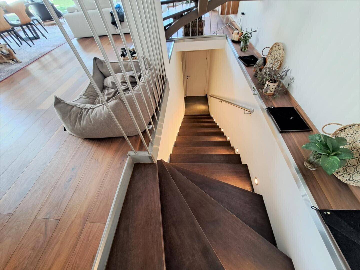 Moderne Treppe mit Holzstufen und Metallgeländer, beleuchtet für Sicherheit.