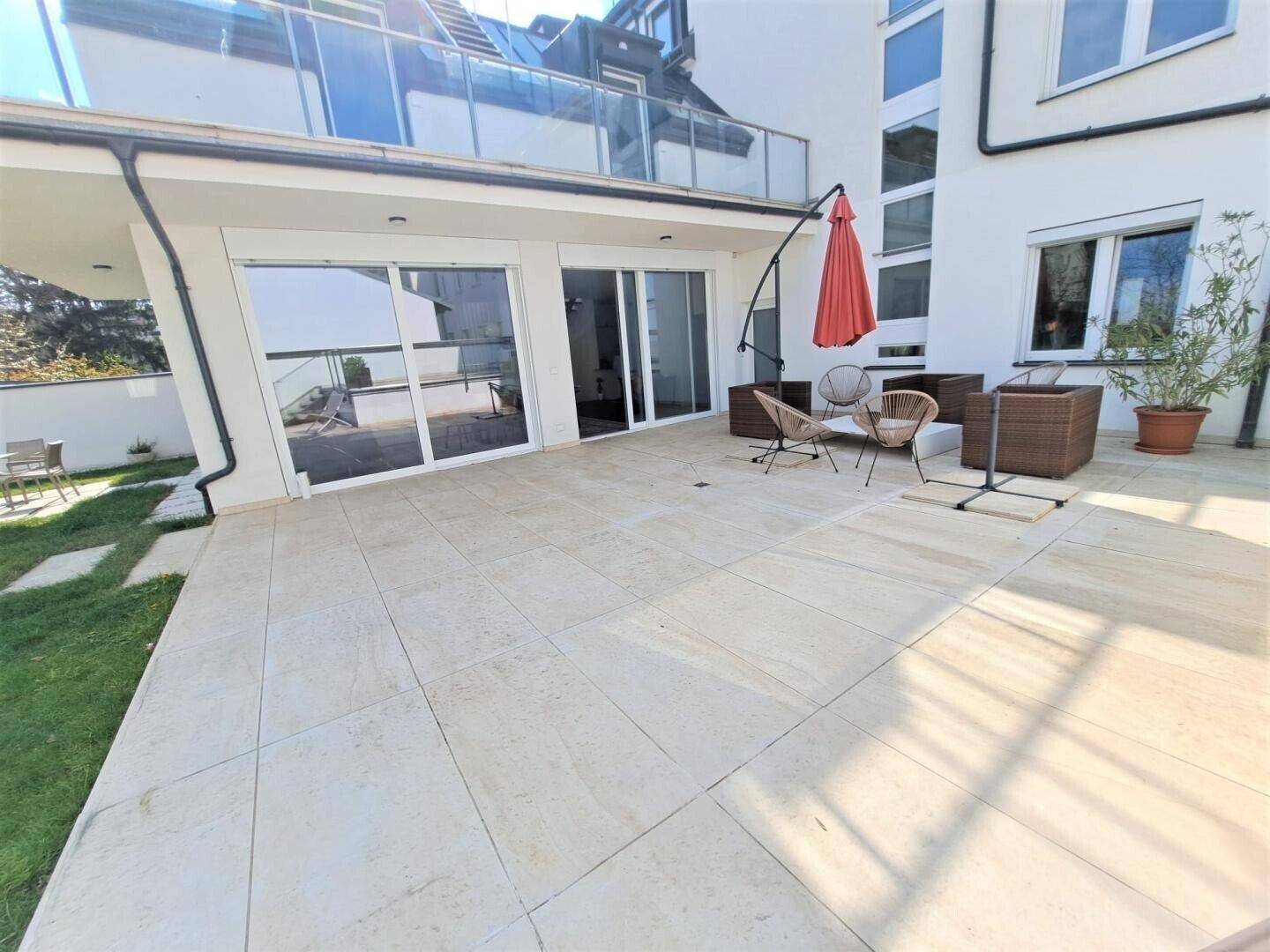 Große, sonnige Terrasse mit Fliesenboden und bequemen Gartenmöbeln.