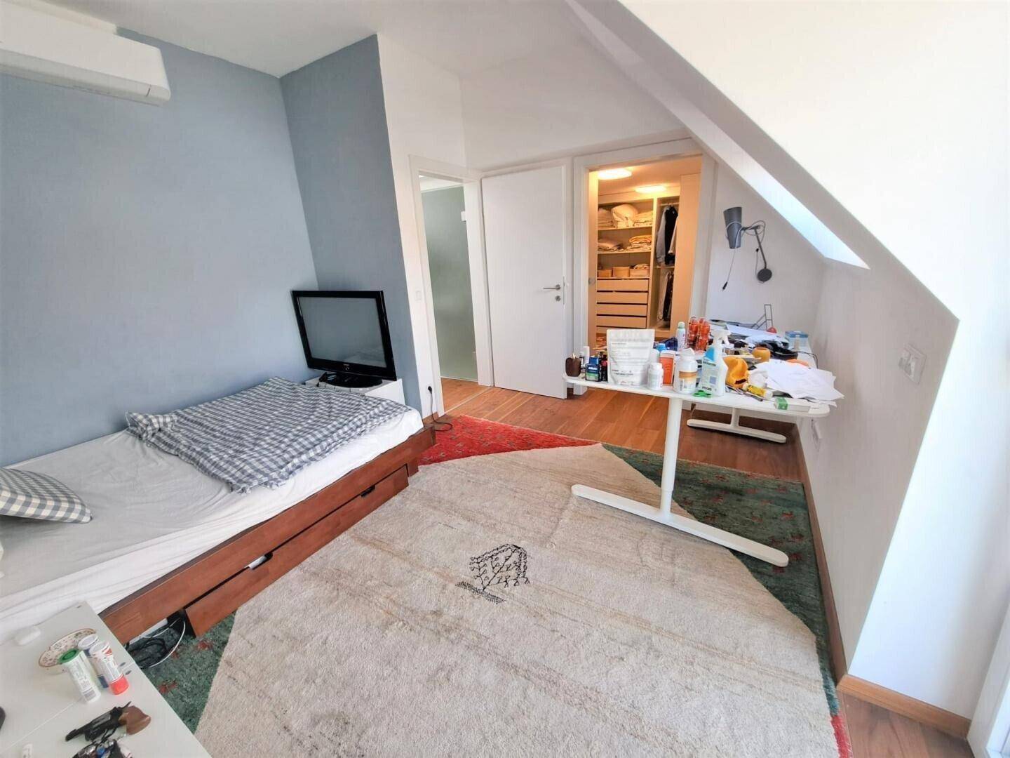 Helles Zimmer mit Dachschräge, Holzboden und Zugang zu einem begehbaren Kleiderschrank.