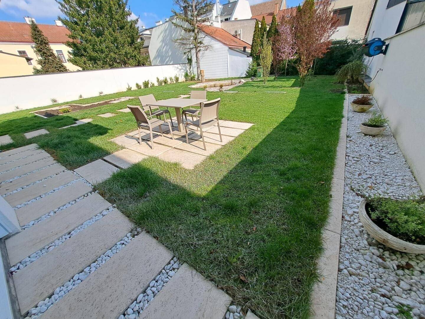 Sonniger Gartenbereich mit Esstisch und Stühlen auf einer gepflasterten Fläche.