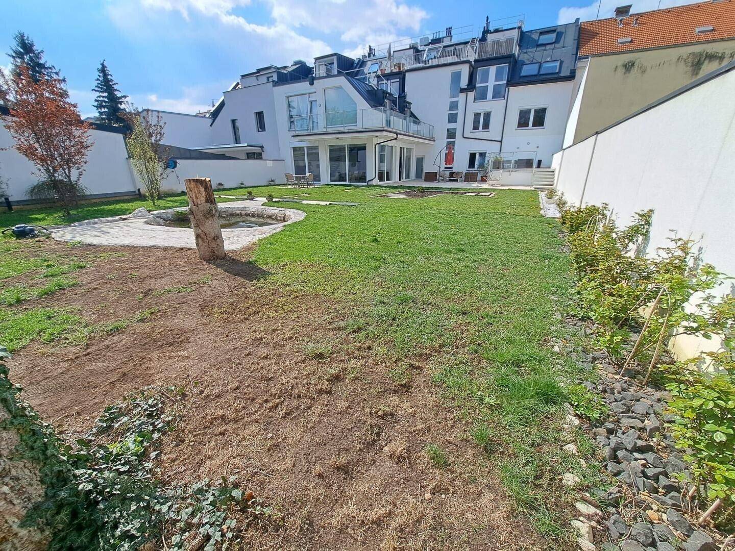Großer Garten mit Rasenfläche, Teich und junger Bepflanzung.