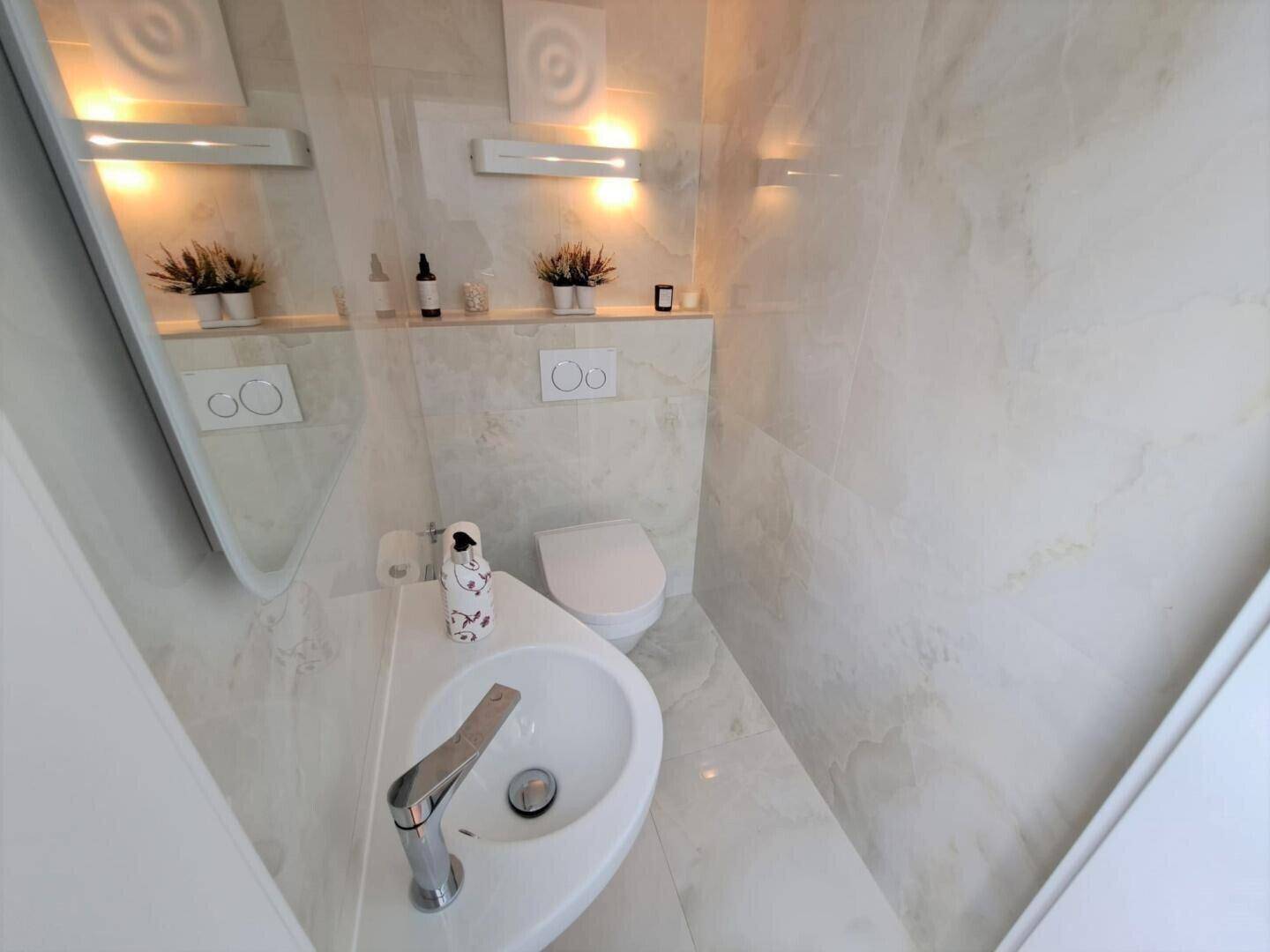 Modernes Gäste-WC mit Wand-WC, kleinem Waschbecken und hellen Fliesen.