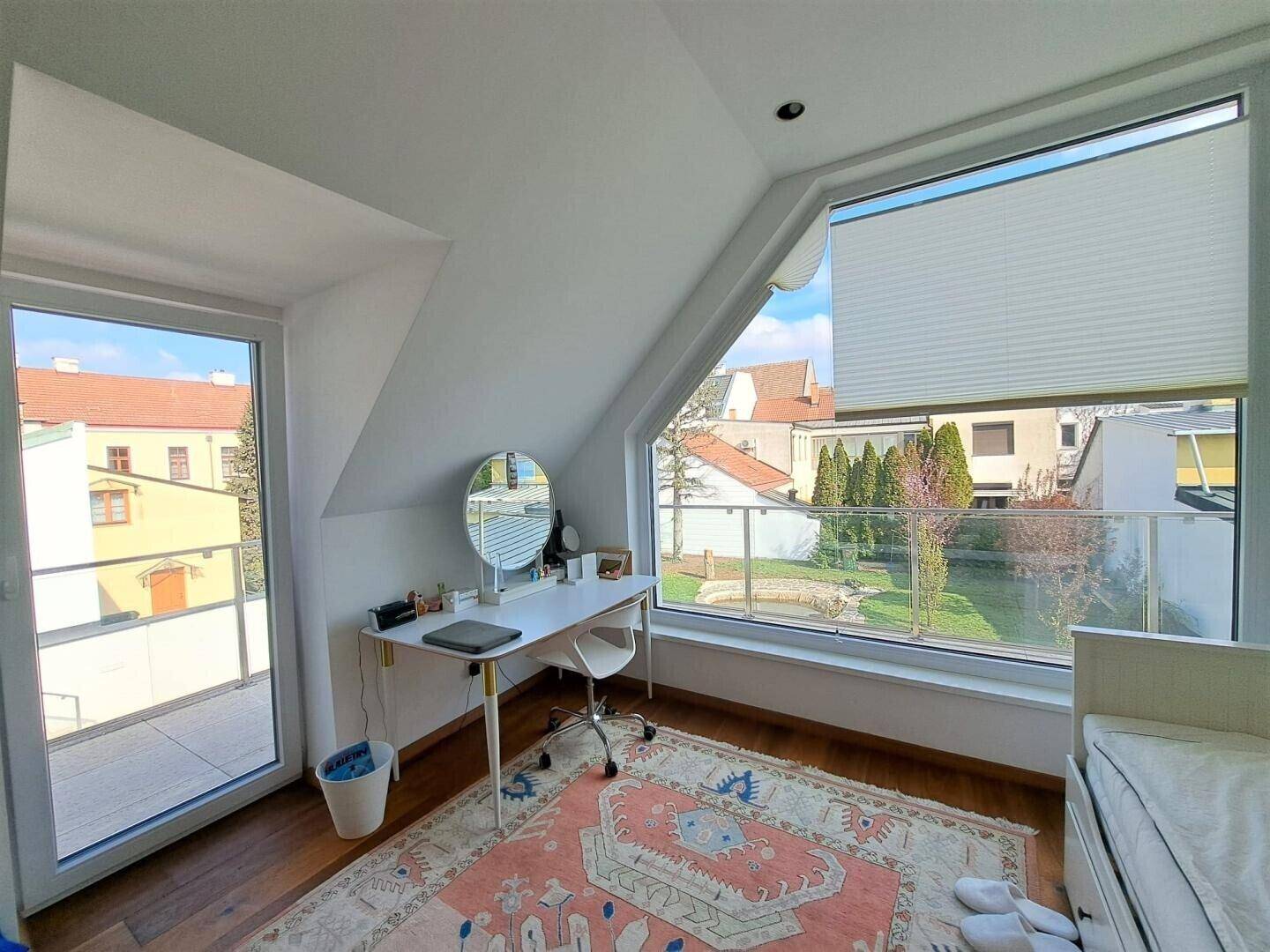 Helles Zimmer mit Dachschräge, Holzboden und Zugang zu einem kleinen Balkon.