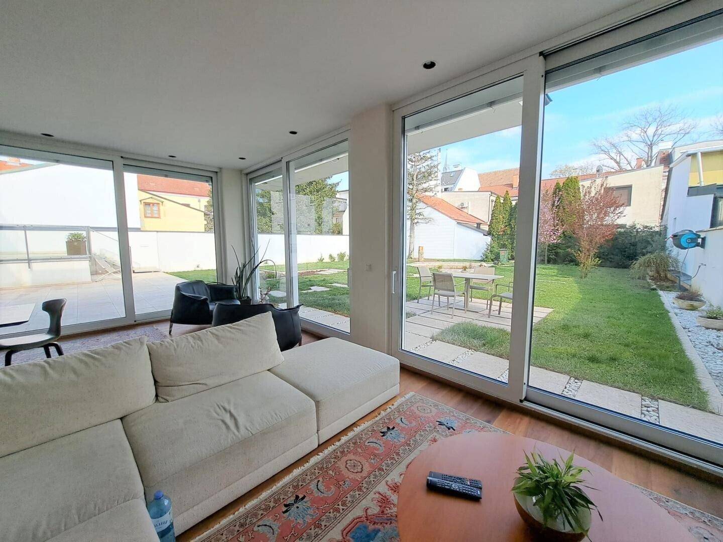 Gemütliches Wohnzimmer mit Sofa, Holzboden und großen Fenstern zum Garten.