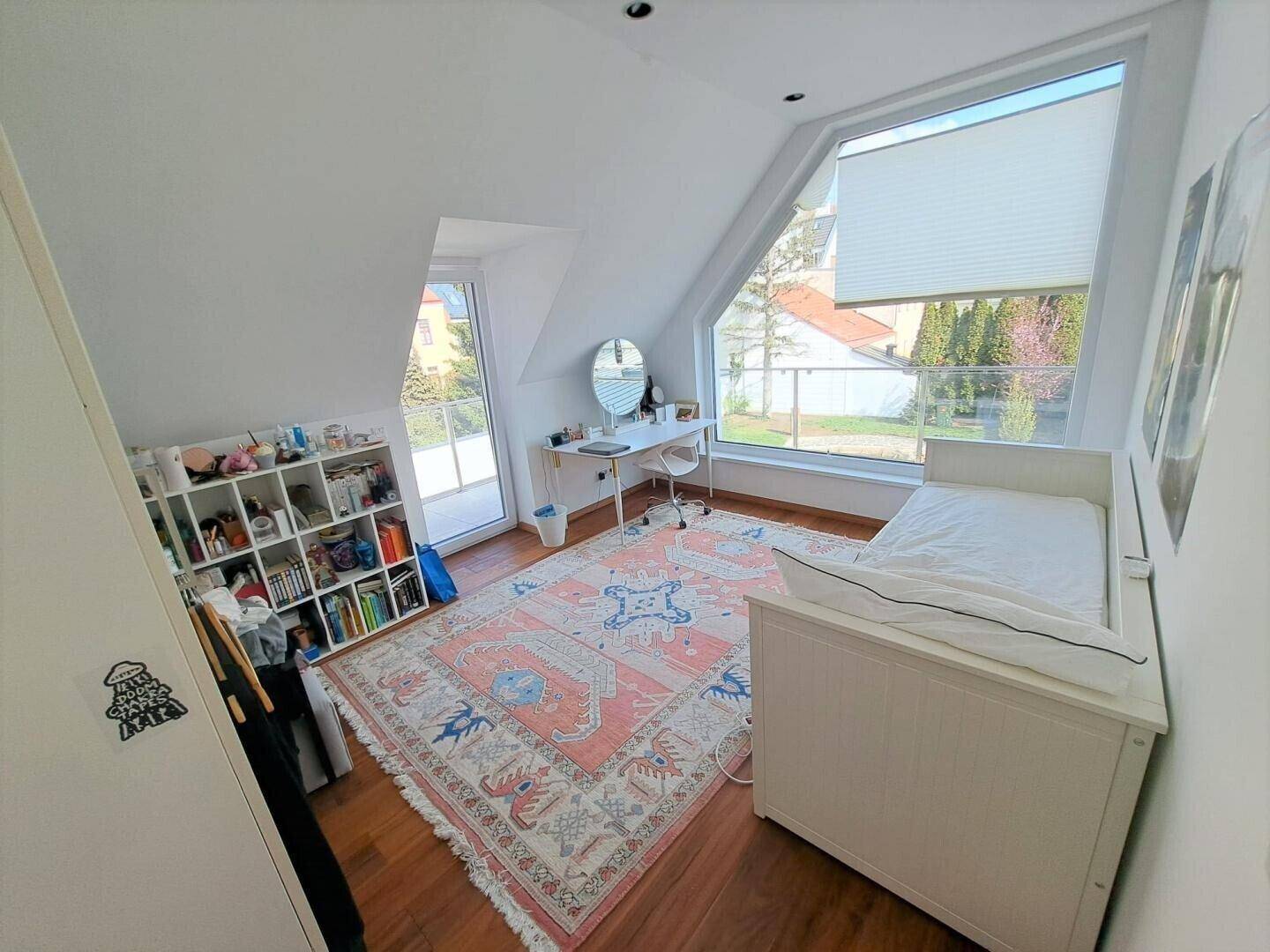 Helles Zimmer mit Dachschräge, Holzboden und großem Fenster mit Blick ins Grüne.