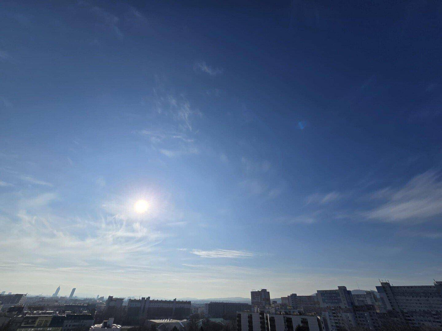 Blauer Himmel mit Sonnenschein und einer weiten Aussicht auf die Stadt am Horizont.