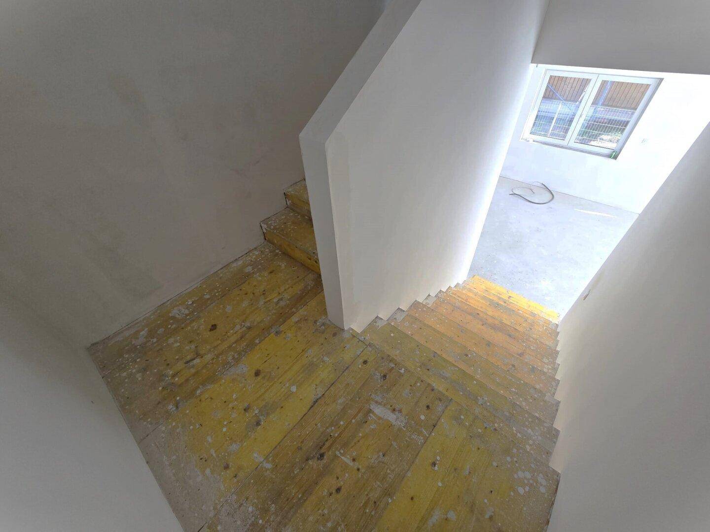 Unfertige Treppe mit gelben Holzstufen, die in den oberen Bereich des Hauses führt.