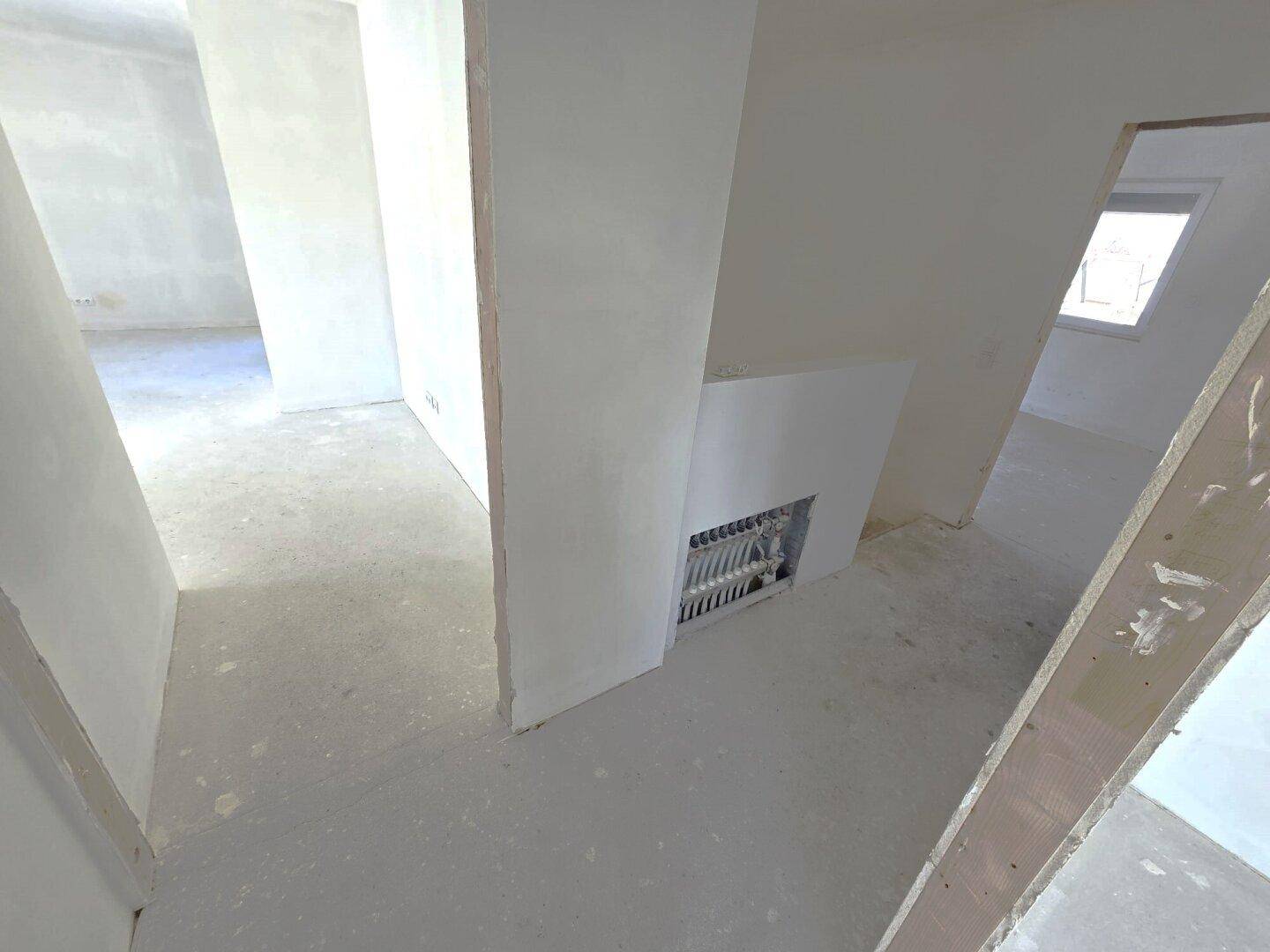 Unfertiger Flurbereich mit Rohinstallationen und Blick in angrenzende Räume.