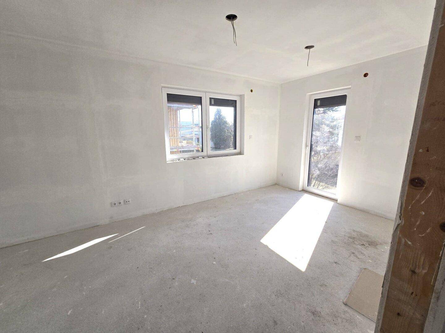 Helles, unfertiges Schlafzimmer mit Fenster und Zugang zu einem möglichen Balkon.