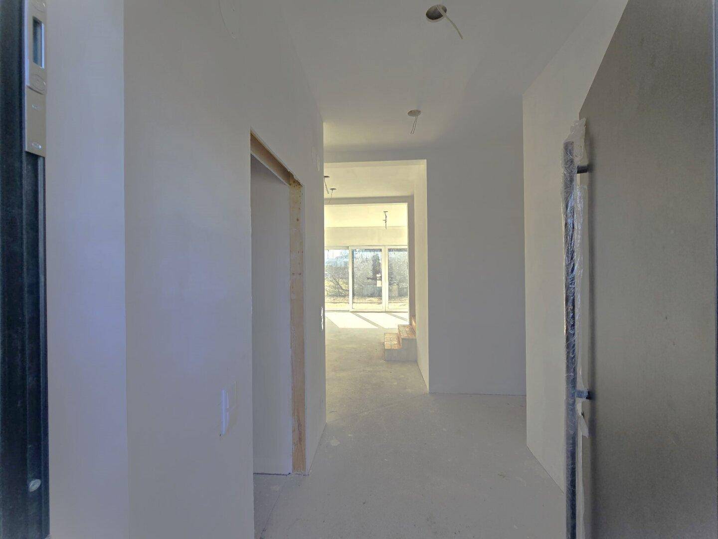 Langer, heller Flur in einem unfertigen Neubau mit Blick in den Wohnbereich.