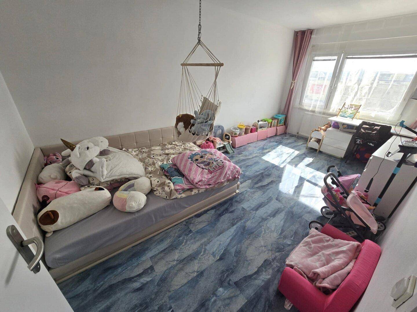 Kinderzimmer mit Bett, Spielzeug und großem Fenster, das viel Tageslicht hereinlässt.
