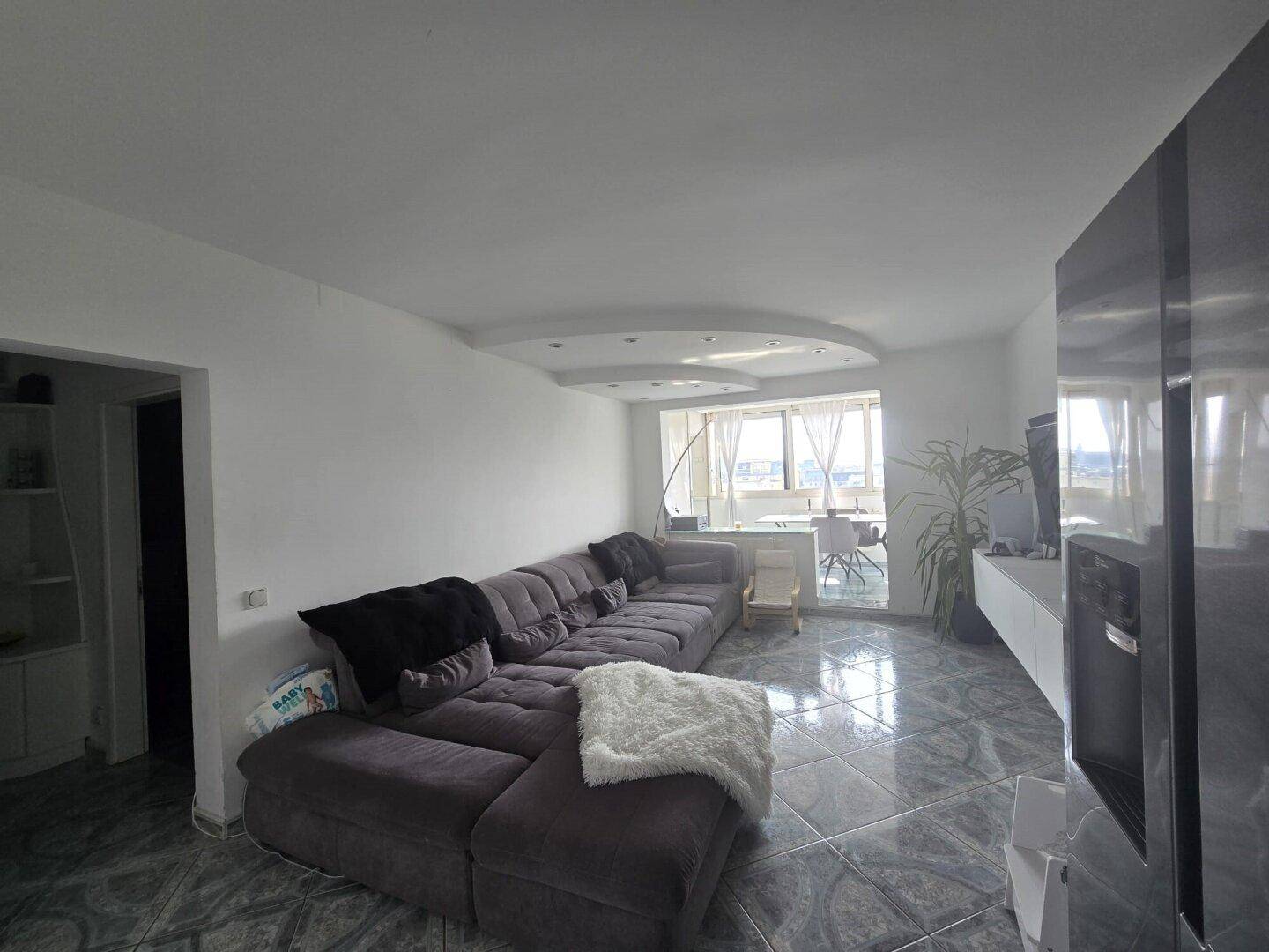 Geräumiges Wohnzimmer mit großem Sofa, Fernseher und dekorativer Deckenbeleuchtung.