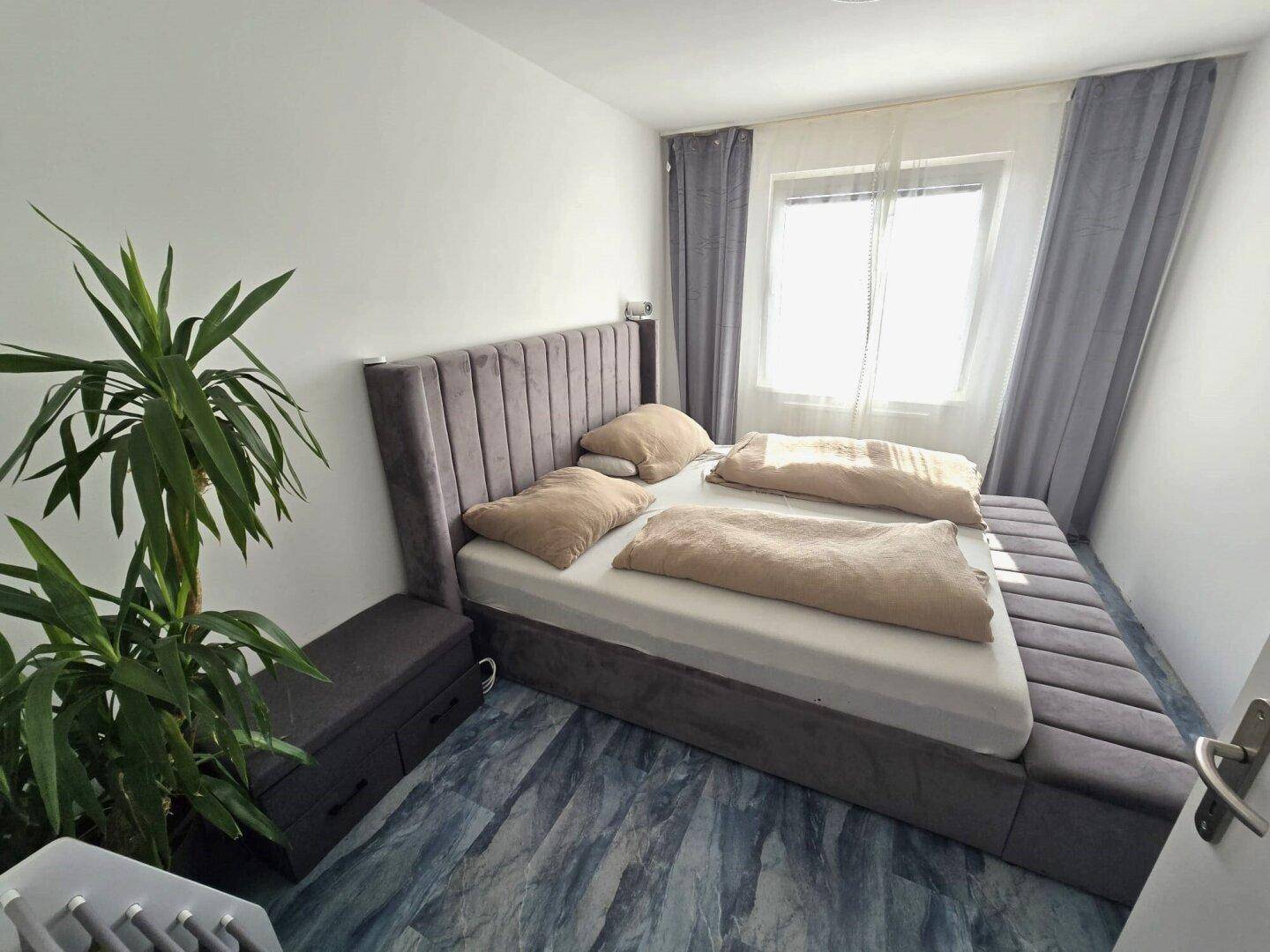 Schlafzimmer mit großem Bett, Nachttischen und Fenster mit Vorhängen.