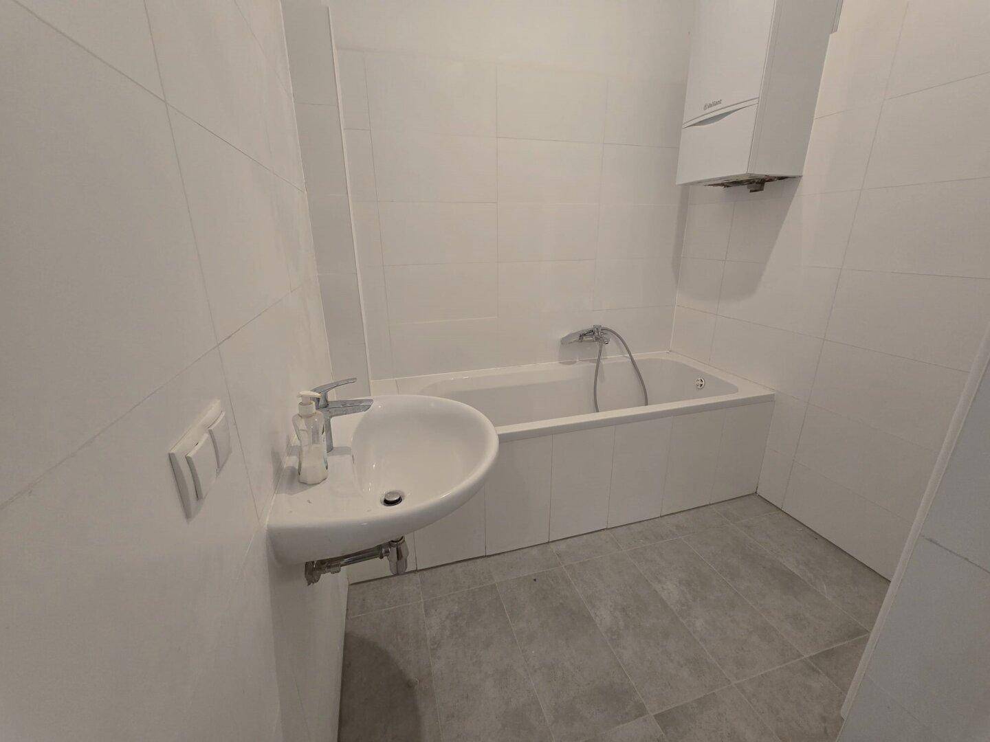 Helles Badezimmer mit Badewanne, Waschbecken und weiß gefliesten Wänden.
