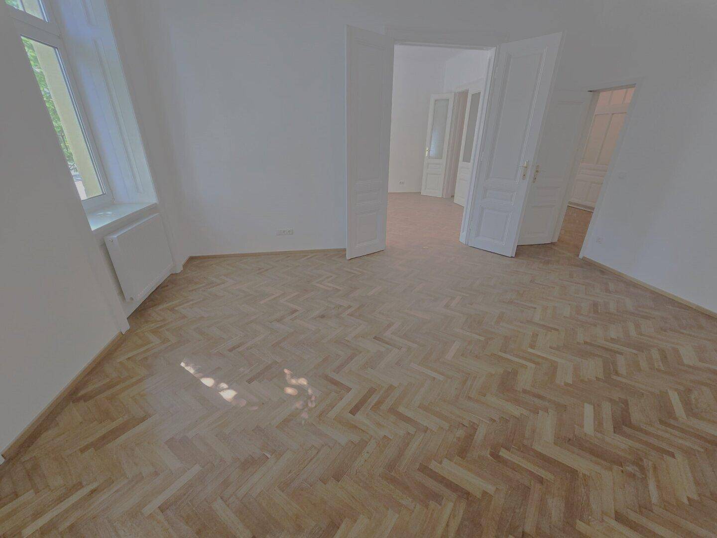 Heller Raum mit Fischgrätparkett und weißen Wänden, ideal für ein Wohn- oder Schlafzimmer.