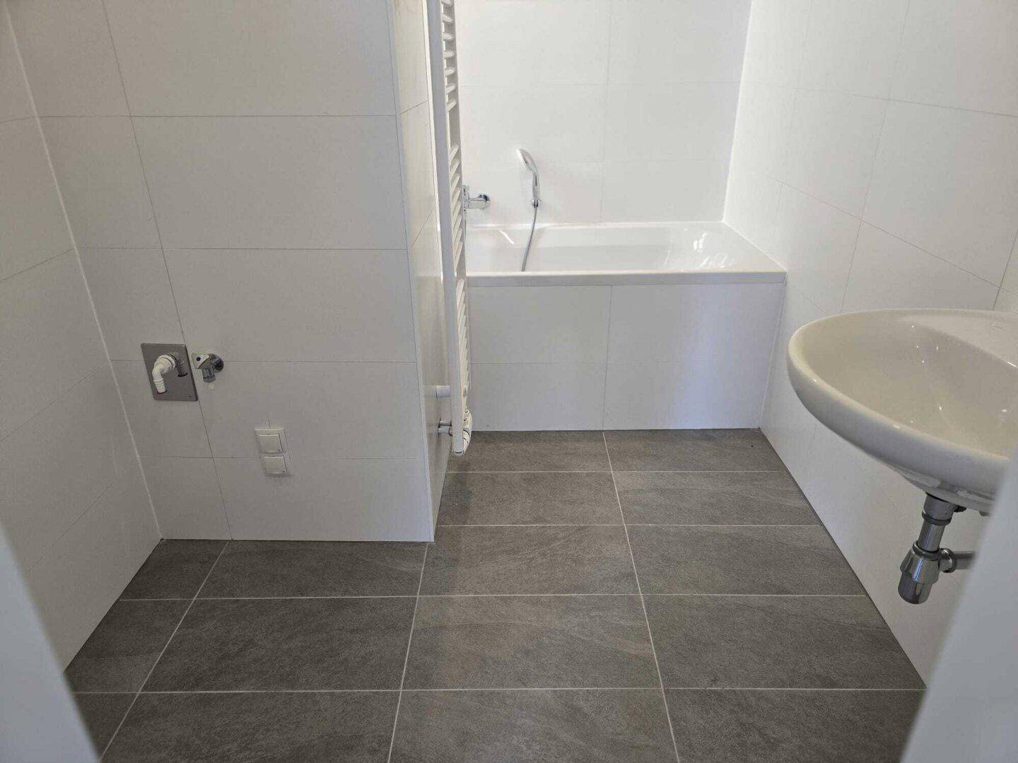 Modernes Badezimmer mit Badewanne, Waschbecken und grauen Bodenfliesen.