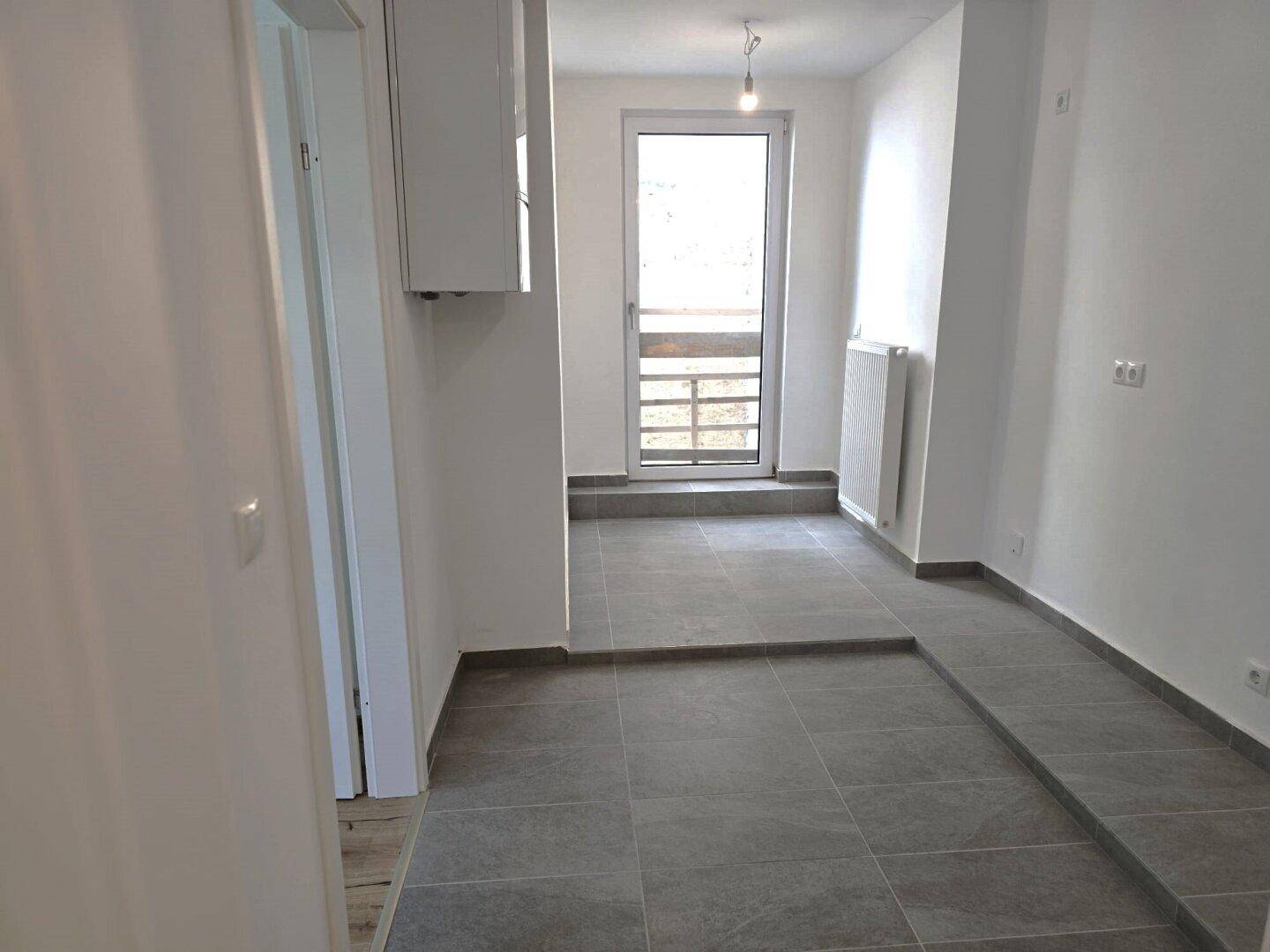 Heller Flur mit grauen Fliesen und Zugang zu einem französischen Balkon.