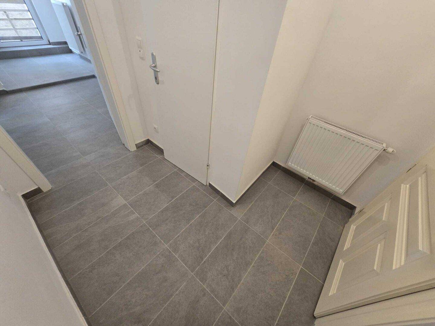 Eingangsbereich mit grauen Bodenfliesen, weiß gestrichenen Wänden und Heizkörper.