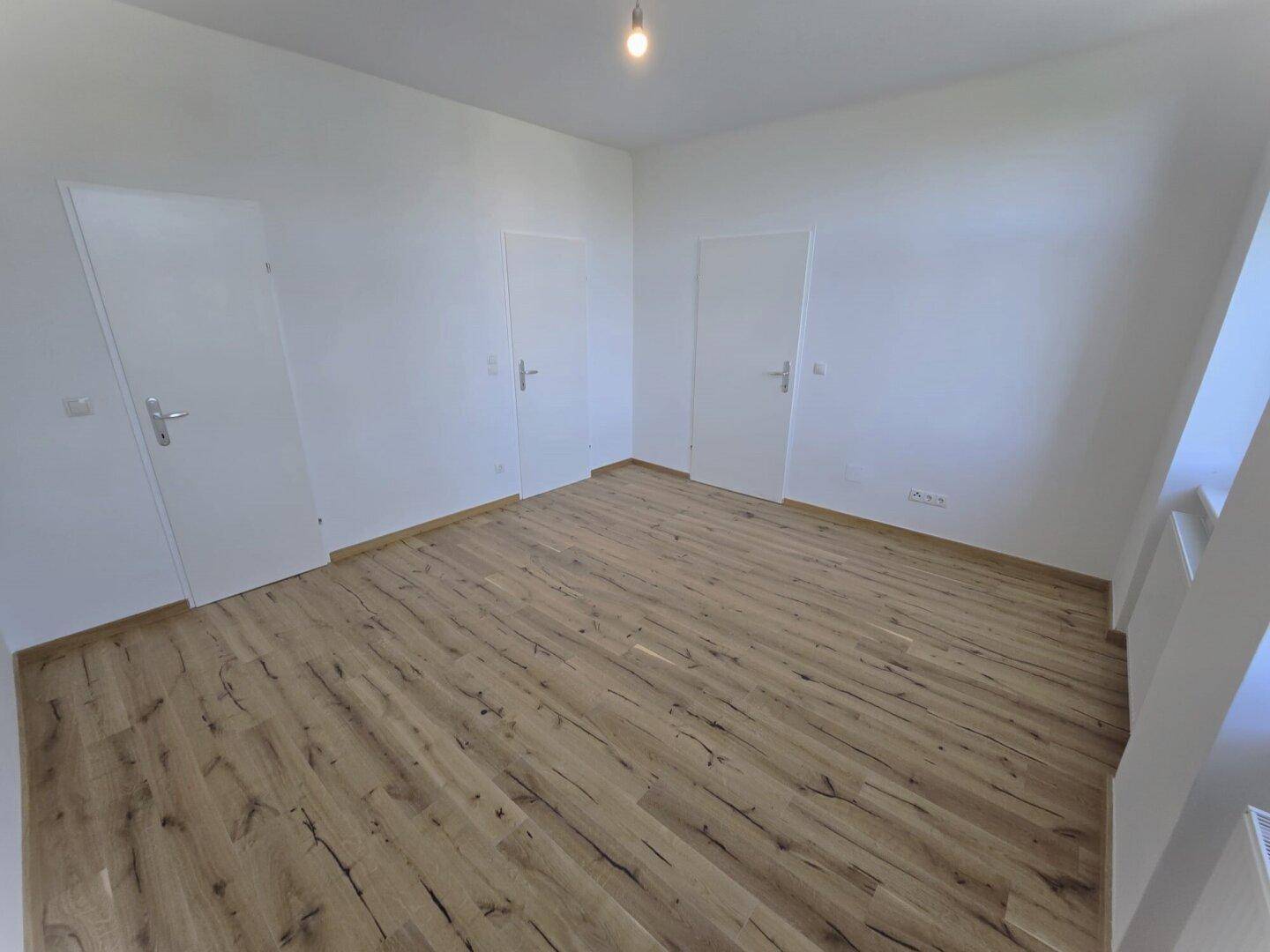 Geräumiges Schlafzimmer mit hellem Laminatboden und zwei weißen Türen.