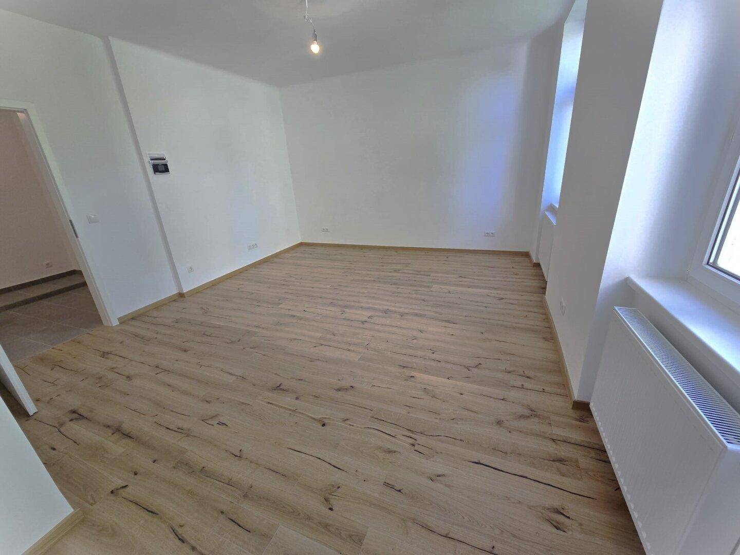 Heller Wohnraum mit Laminatboden und Zugang zu einem weiteren Bereich der Wohnung.