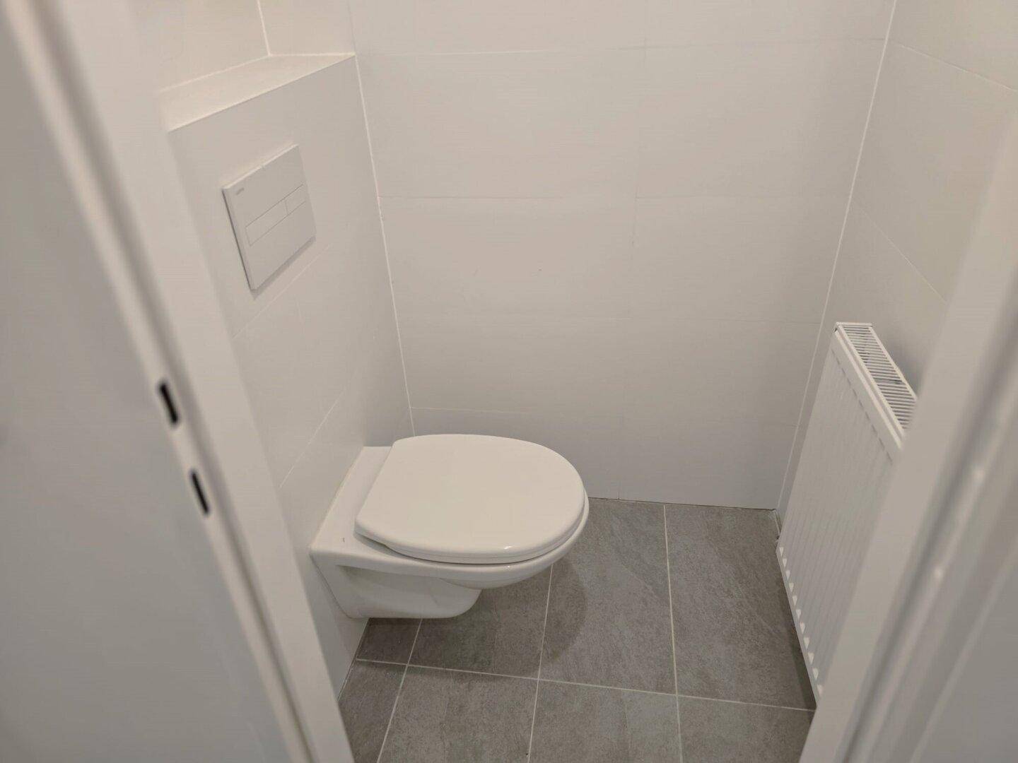Kleines, modernes WC mit wandhängender Toilette und grauen Bodenfliesen.