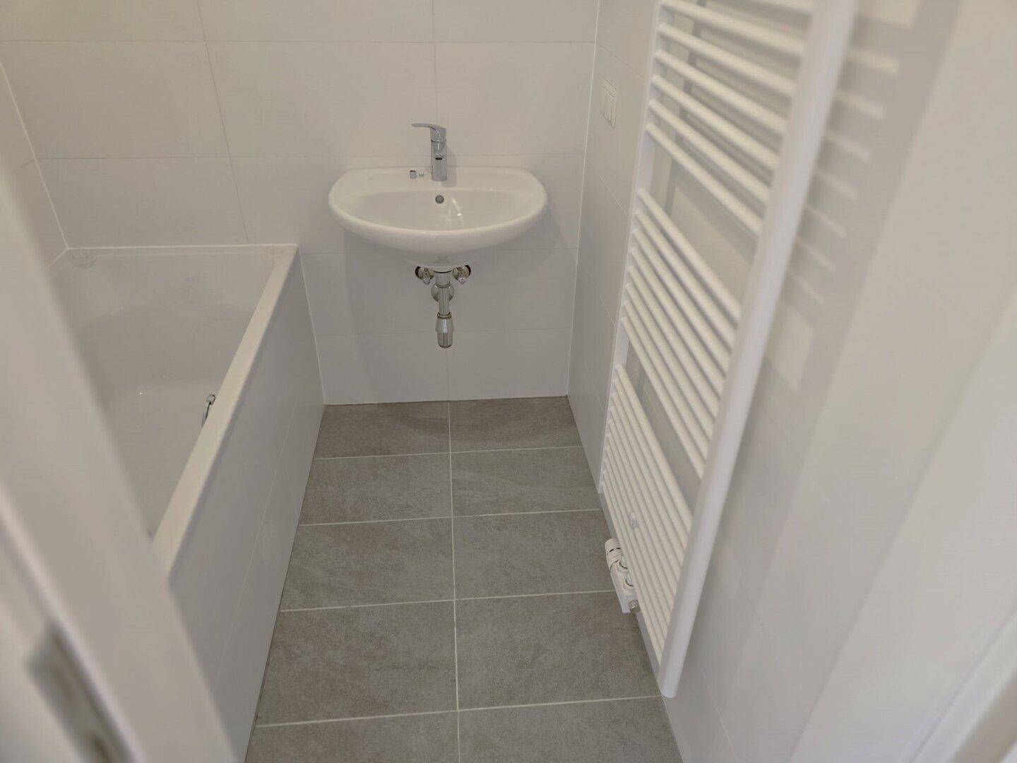 Helles Badezimmer mit Badewanne, Waschbecken und beheiztem Handtuchhalter.