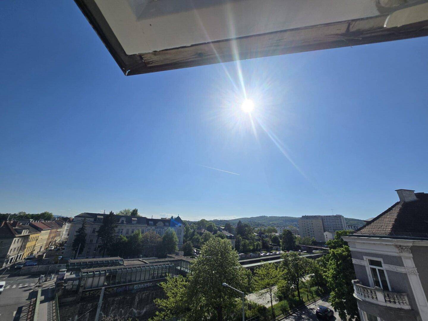 Sonniger Ausblick auf die Stadt und grüne Umgebung von einem Fenster aus.