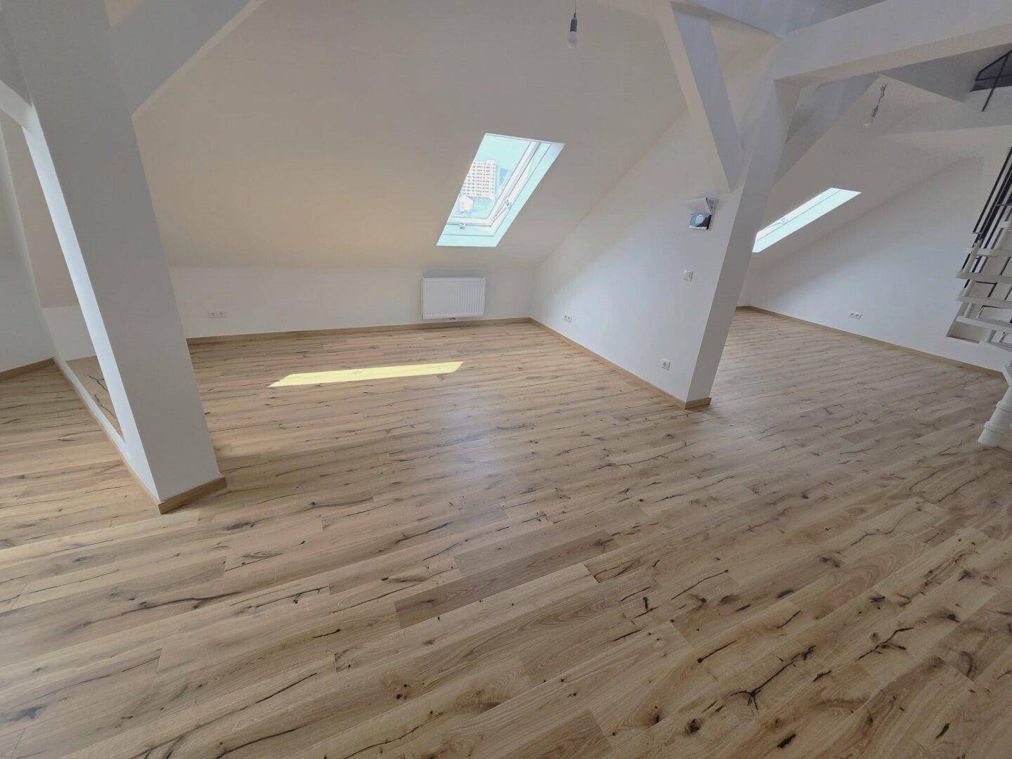 Geräumiger Dachboden-Wohnbereich mit Holzboden und schrägen Decken mit Dachfenstern.