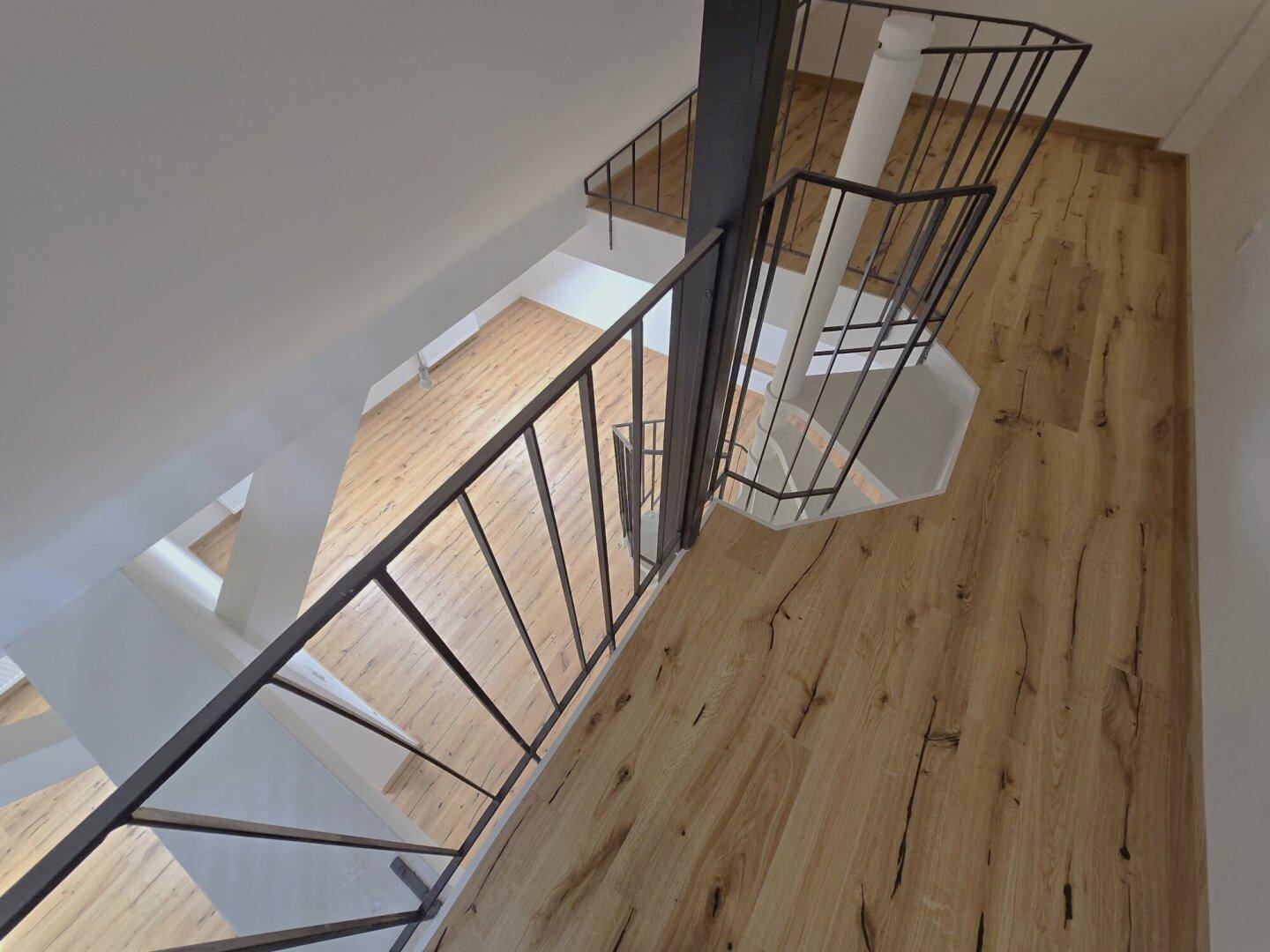 Oberer Flurbereich mit schwarzem Geländer und Blick auf die Wendeltreppe im Dachgeschoss.
