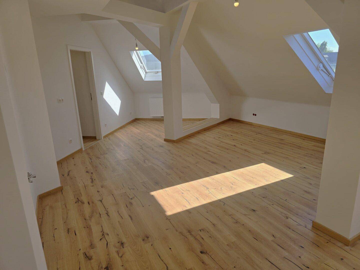 Lichtdurchfluteter Dachbodenraum mit Holzboden, schrägen Wänden und mehreren Dachfenstern.