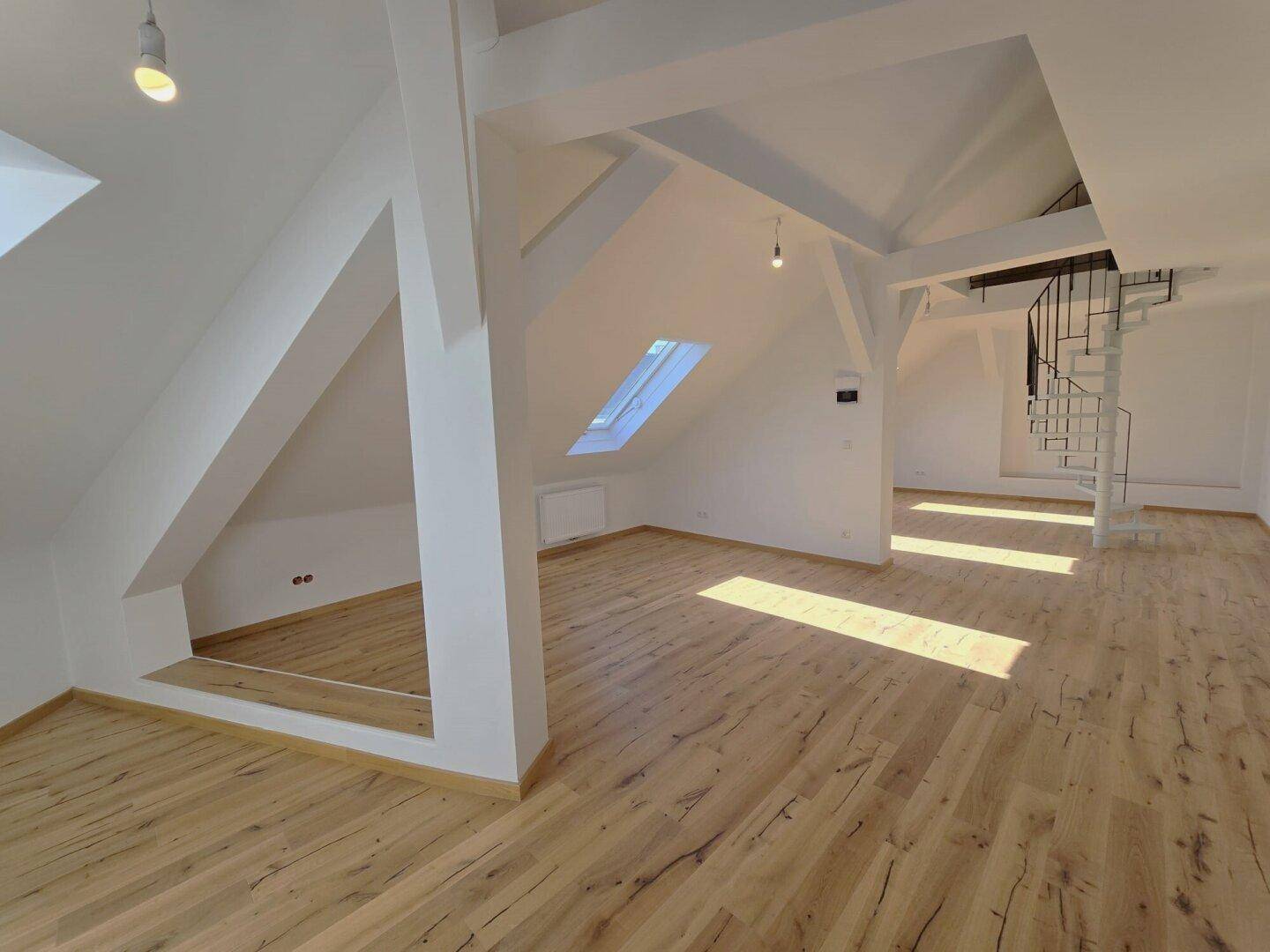Heller Dachbodenraum mit sichtbaren Holzbalken, Dachfenstern und Wendeltreppe.