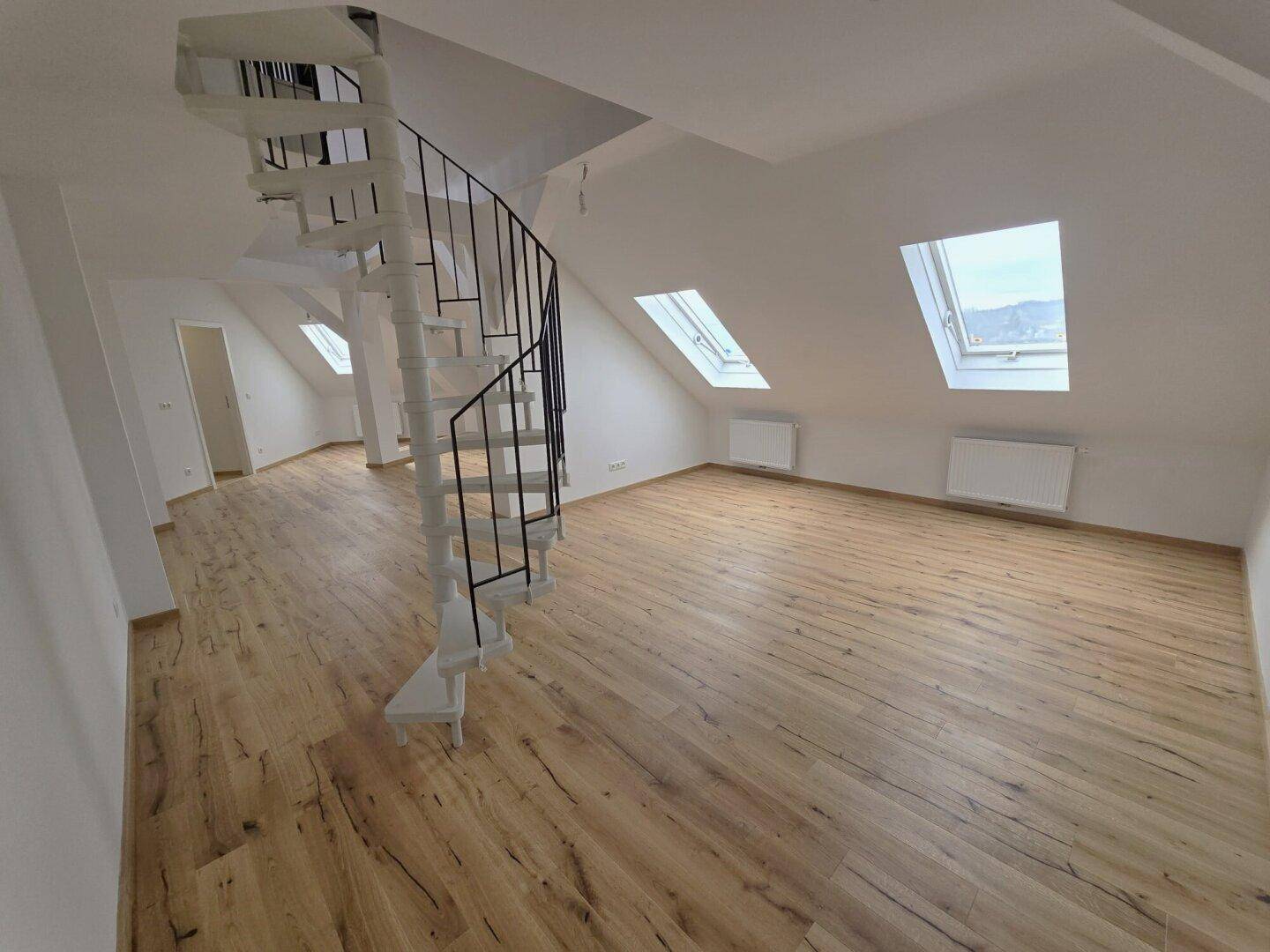 Geräumiger Dachboden-Wohnbereich mit Wendeltreppe, Holzboden und Dachfenstern.