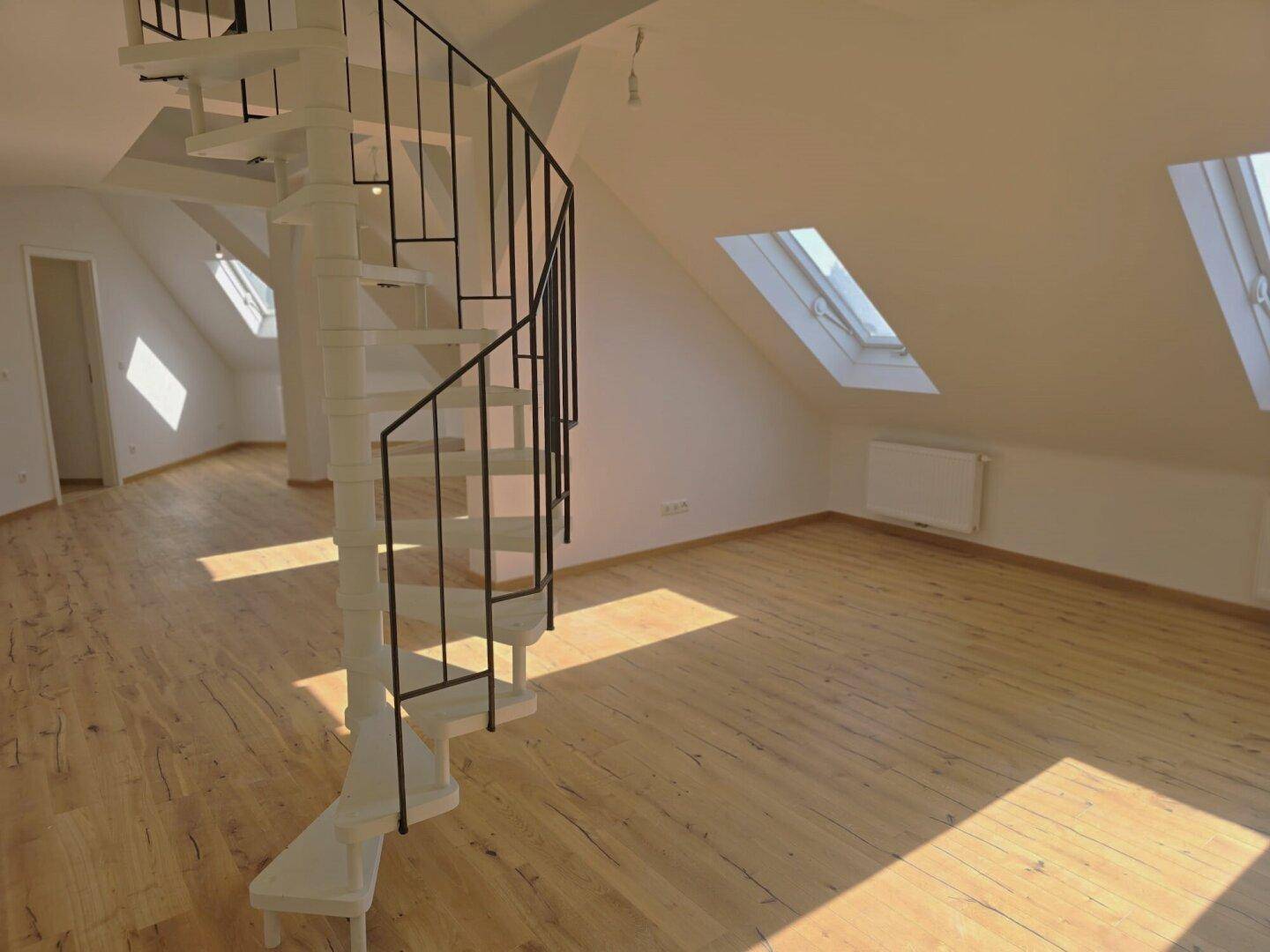 Geräumiger Dachboden-Wohnbereich mit Wendeltreppe, Holzboden und Dachfenstern.