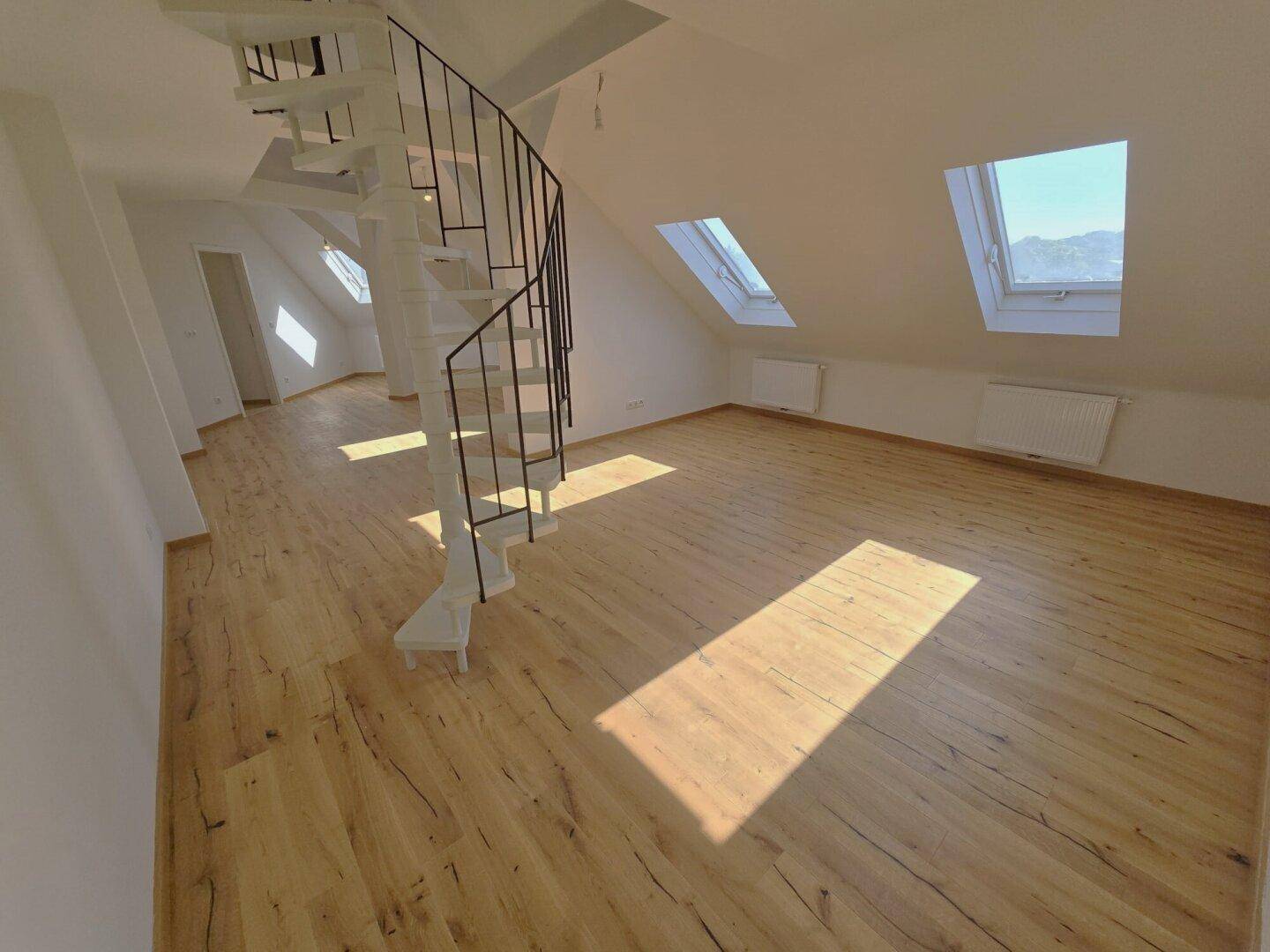 Lichtdurchfluteter Dachbodenraum mit Wendeltreppe, Holzboden und sonnigen Dachfenstern.