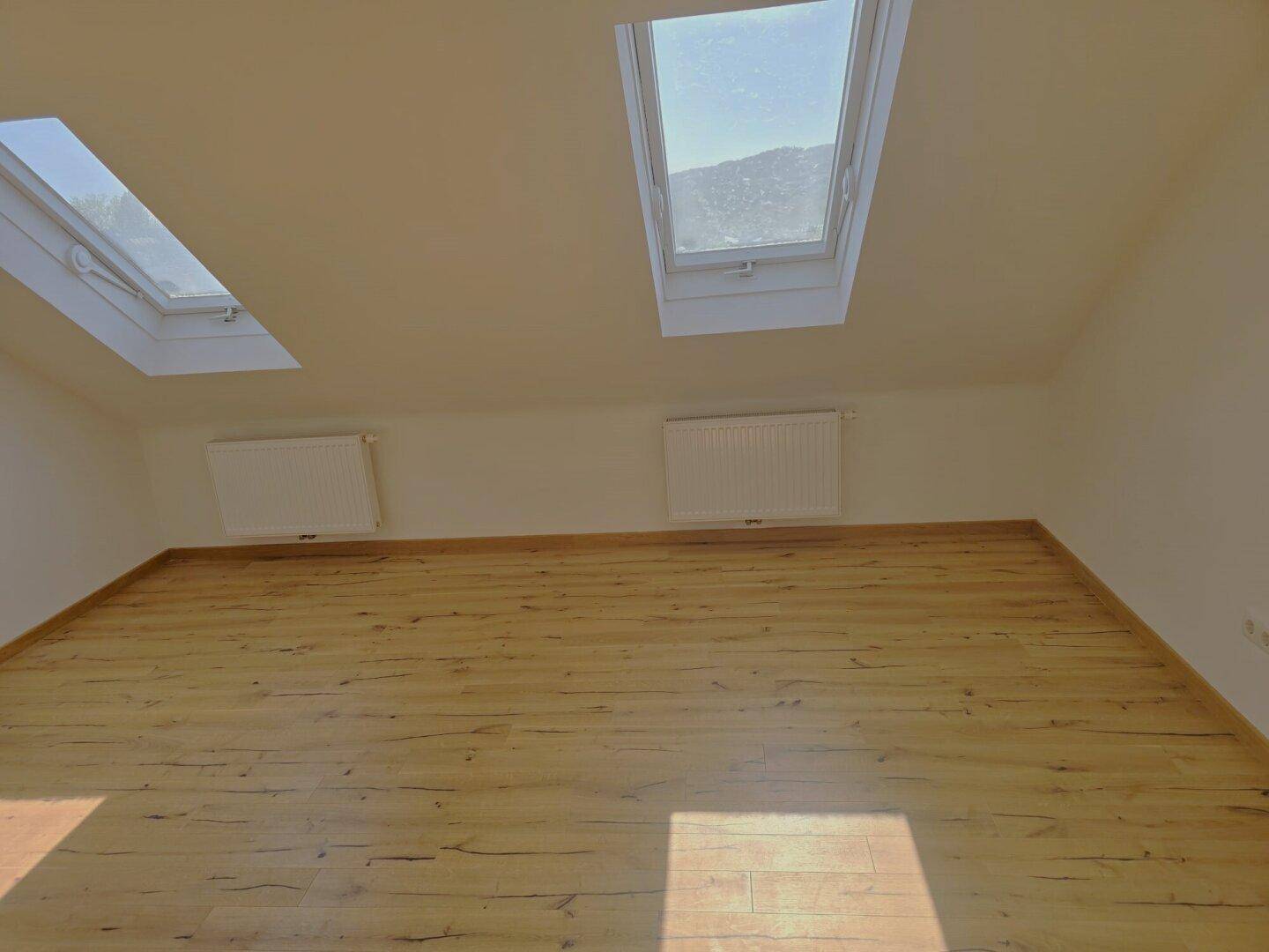 Heller Dachbodenraum mit Laminatboden, Heizkörpern und zwei großen Dachfenstern.