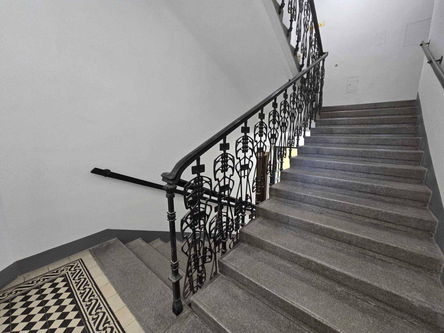 Historisches Treppenhaus mit Steinstufen, kunstvollem schmiedeeisernem Geländer und gemusterten Fliesen.