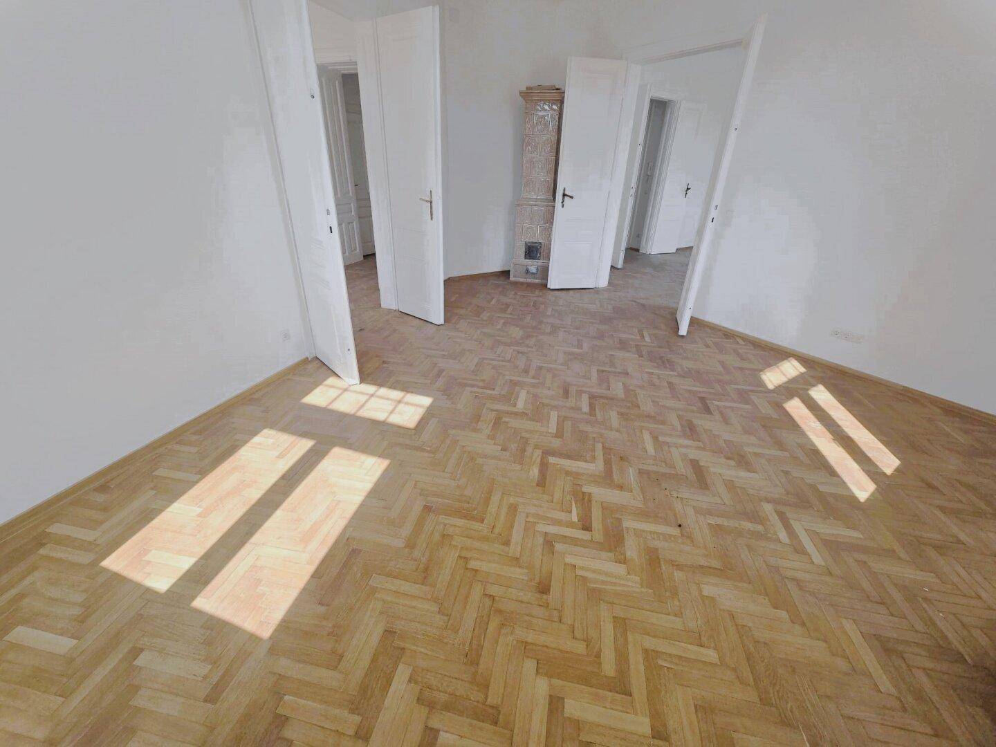 Zentraler Raum mit Fischgrätparkett und mehreren offenen Türen, der verschiedene Bereiche der Wohnung verbindet.