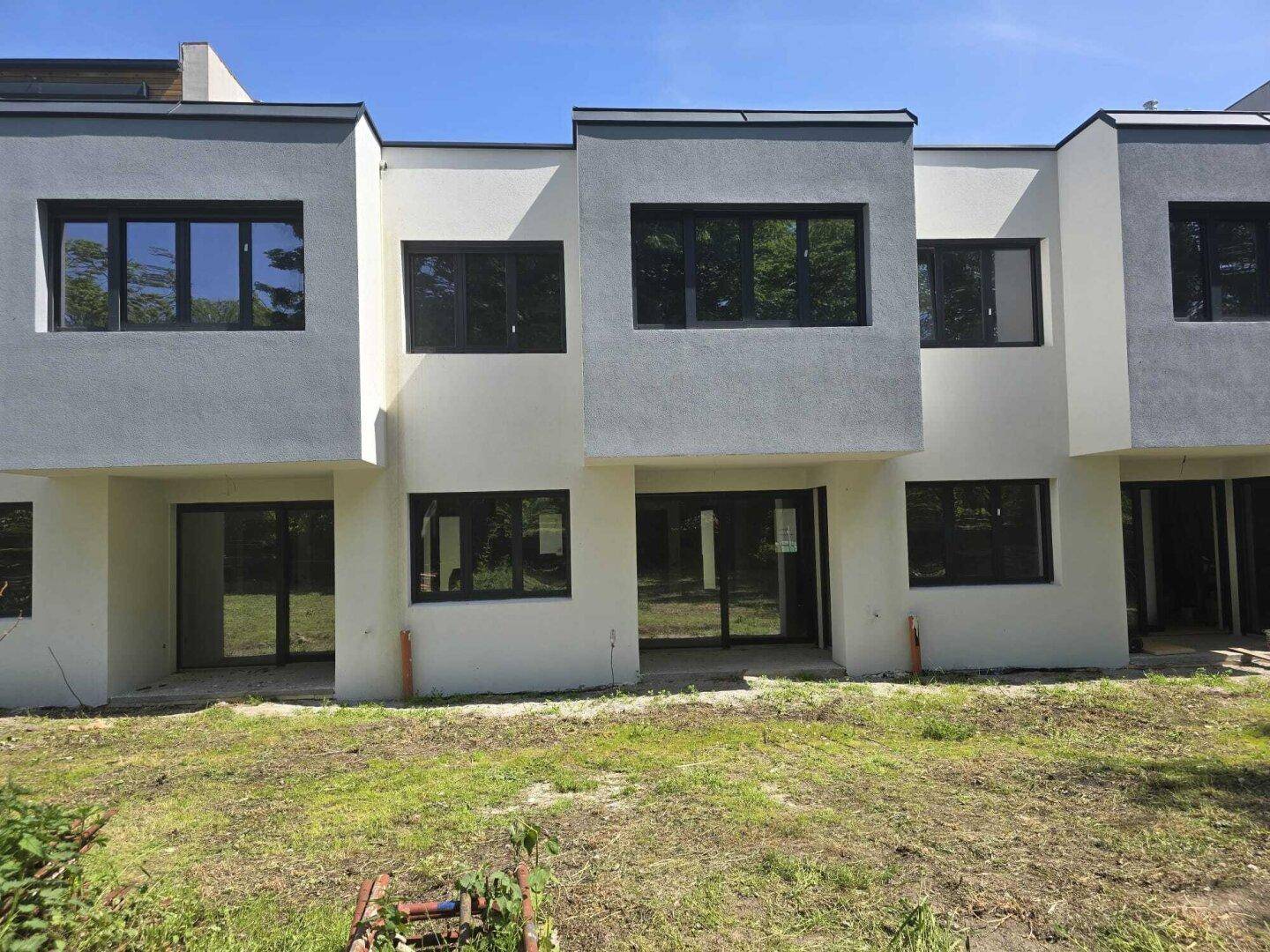 Rückseite des Neubaus mit großen Glasfronten und Zugang zu den zukünftigen Terrassenbereichen.