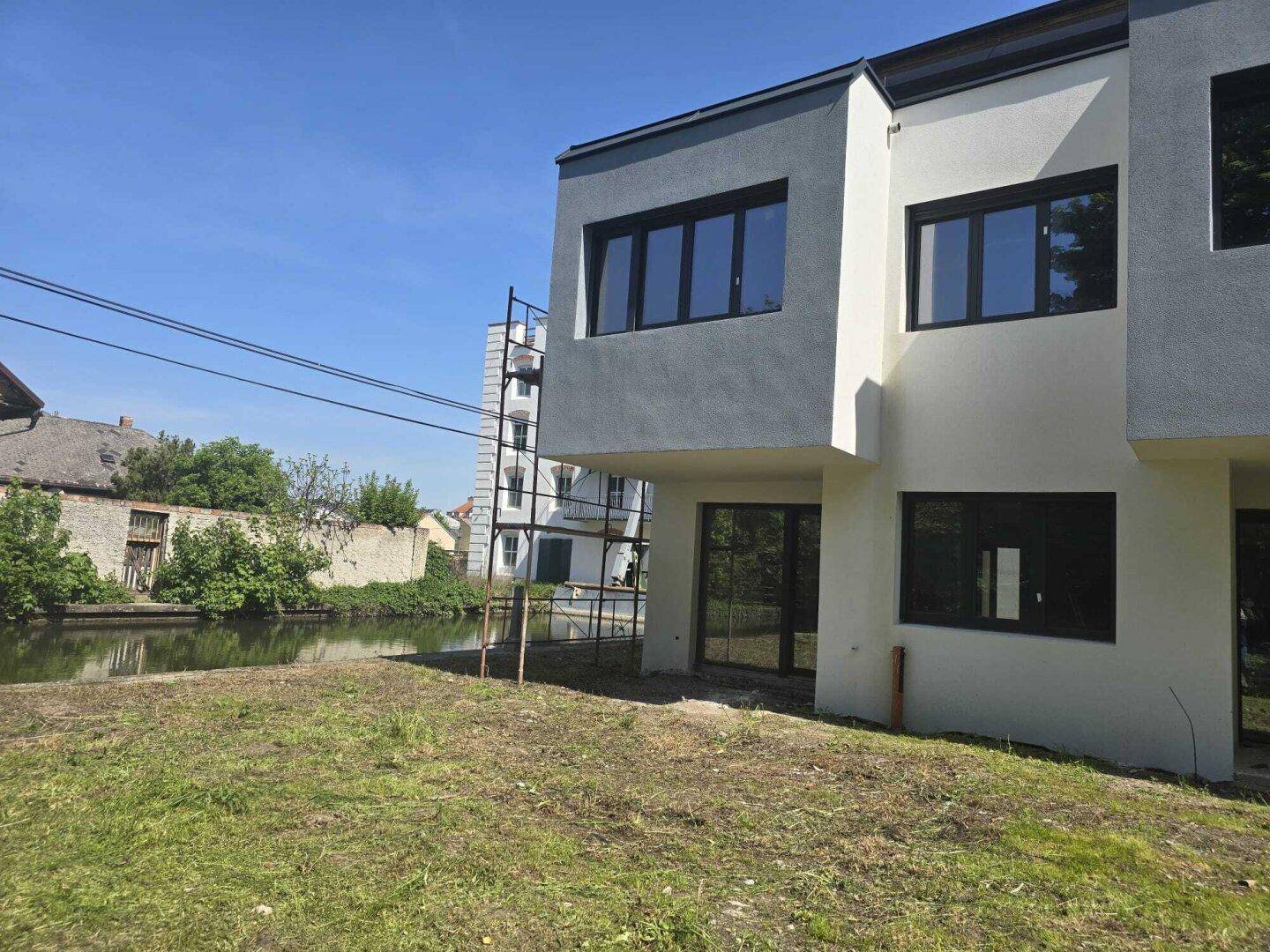 Neubau-Fassade mit modernen Fenstern und Blick auf den angrenzenden Flusslauf.