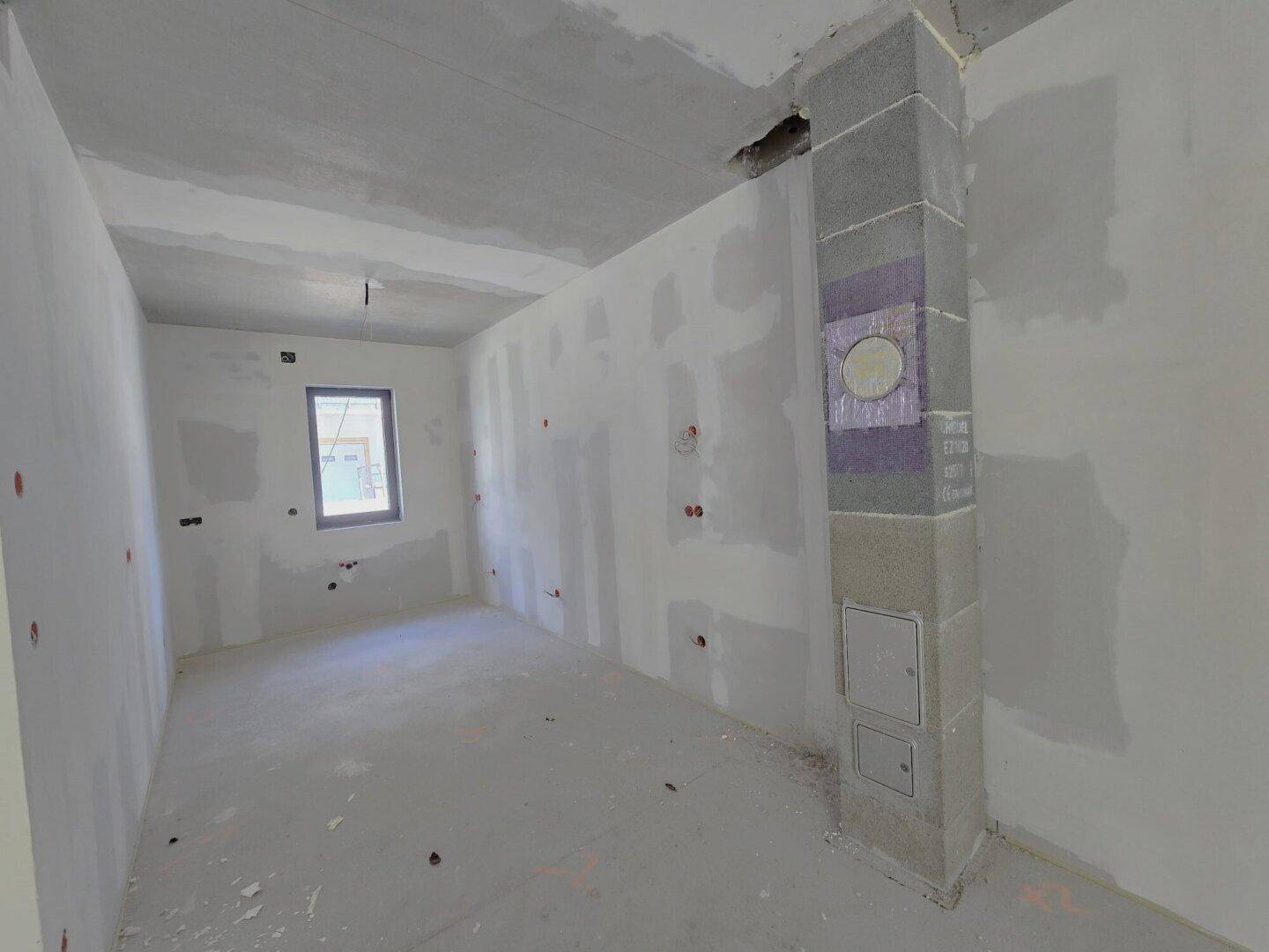 Unfertiger Innenraum eines Neubaus mit verputzten Wänden und sichtbarer Betondecke.