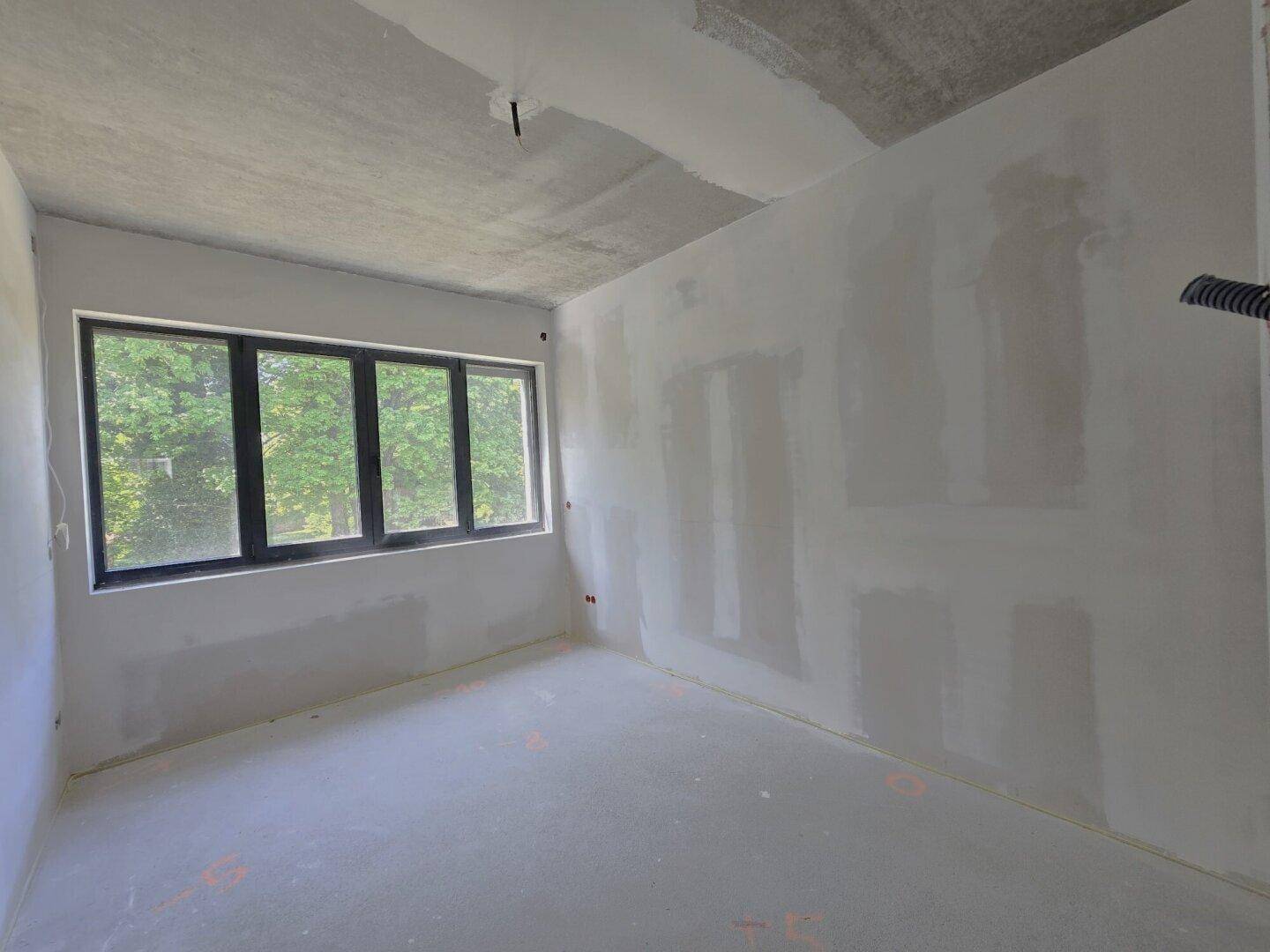 Heller Raum im Rohbau mit großem Fenster, das viel Tageslicht hereinlässt.