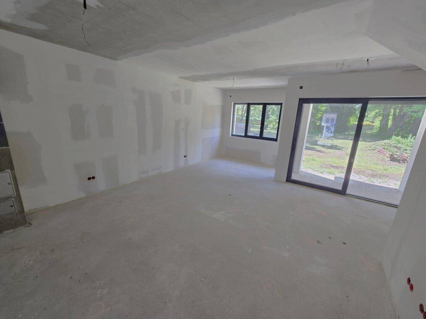 Heller Wohnraum im Rohbau mit großen Fenstern und Schiebetüren zum Außenbereich.