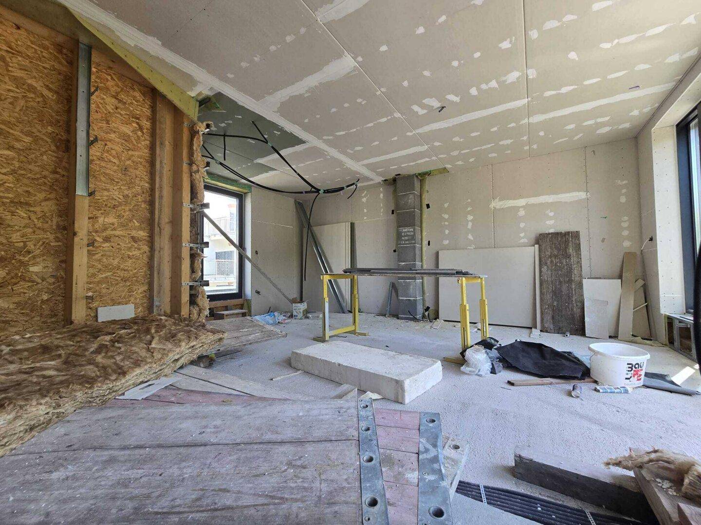 Innenraum im Bau mit sichtbarer Isolierung und Baumaterialien, bereit für den weiteren Ausbau.