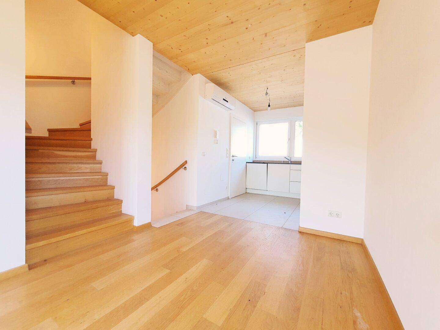 Offener Wohnbereich mit Holztreppe und Zugang zu einer modernen Küche.