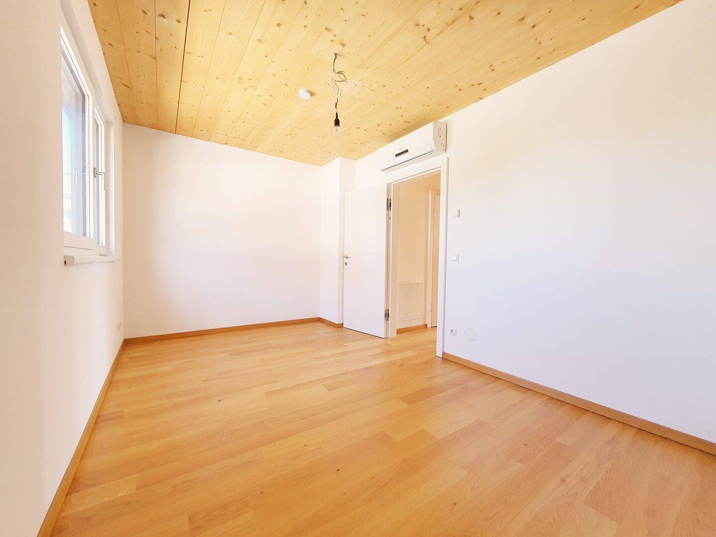 Helles Zimmer mit Holzboden, Holzbalkendecke und Klimaanlage.