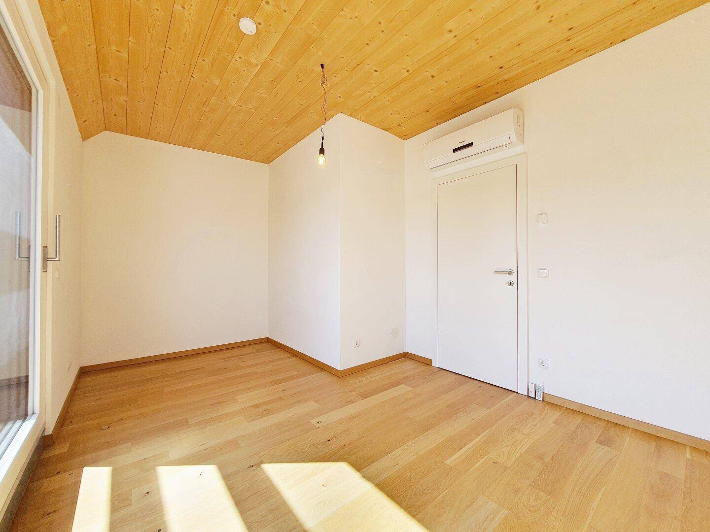 Geräumiges Zimmer mit Holzboden, Holzbalkendecke und viel natürlichem Licht.