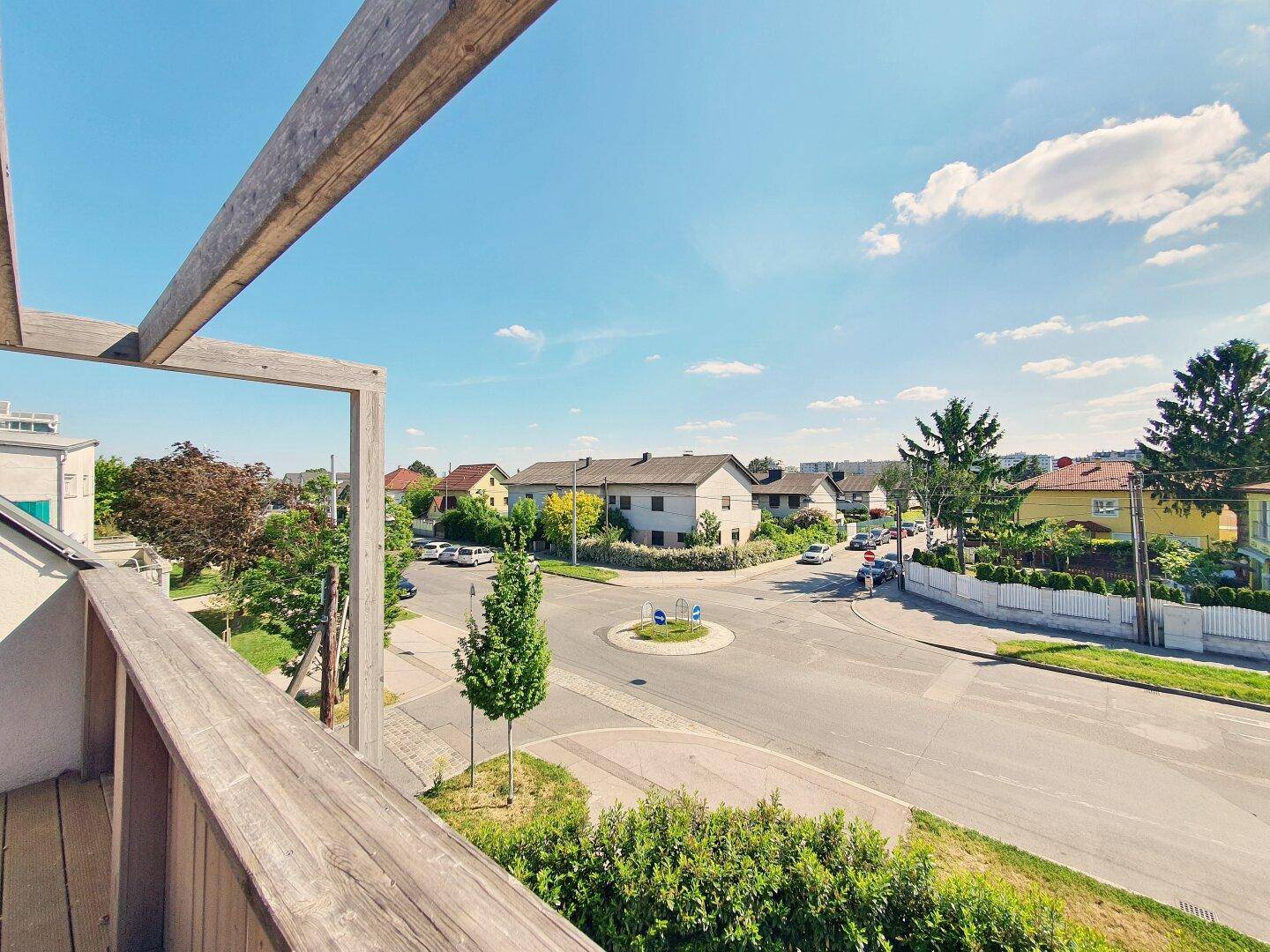 Blick von einem Balkon auf die umliegende Wohngegend mit Straßen und Bäumen.
