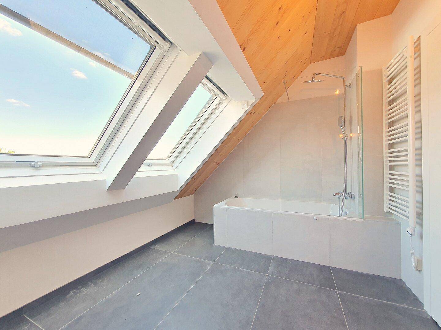 Helles Badezimmer im Dachgeschoss mit Badewanne, Dachfenstern und Holzbalkendecke.